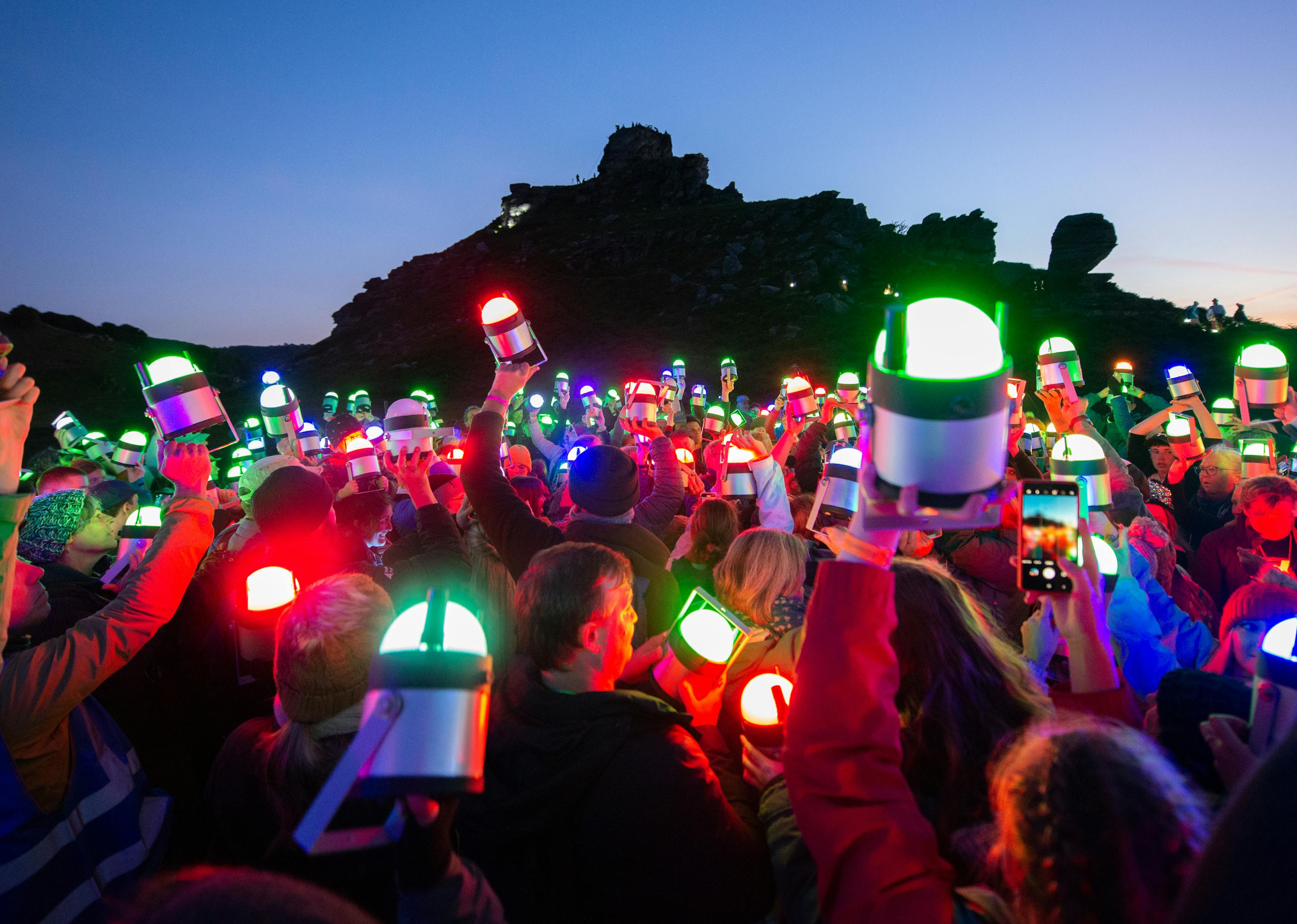 Lumenators holding up their geolights into the sky, lit in different colours as the sun goes down
