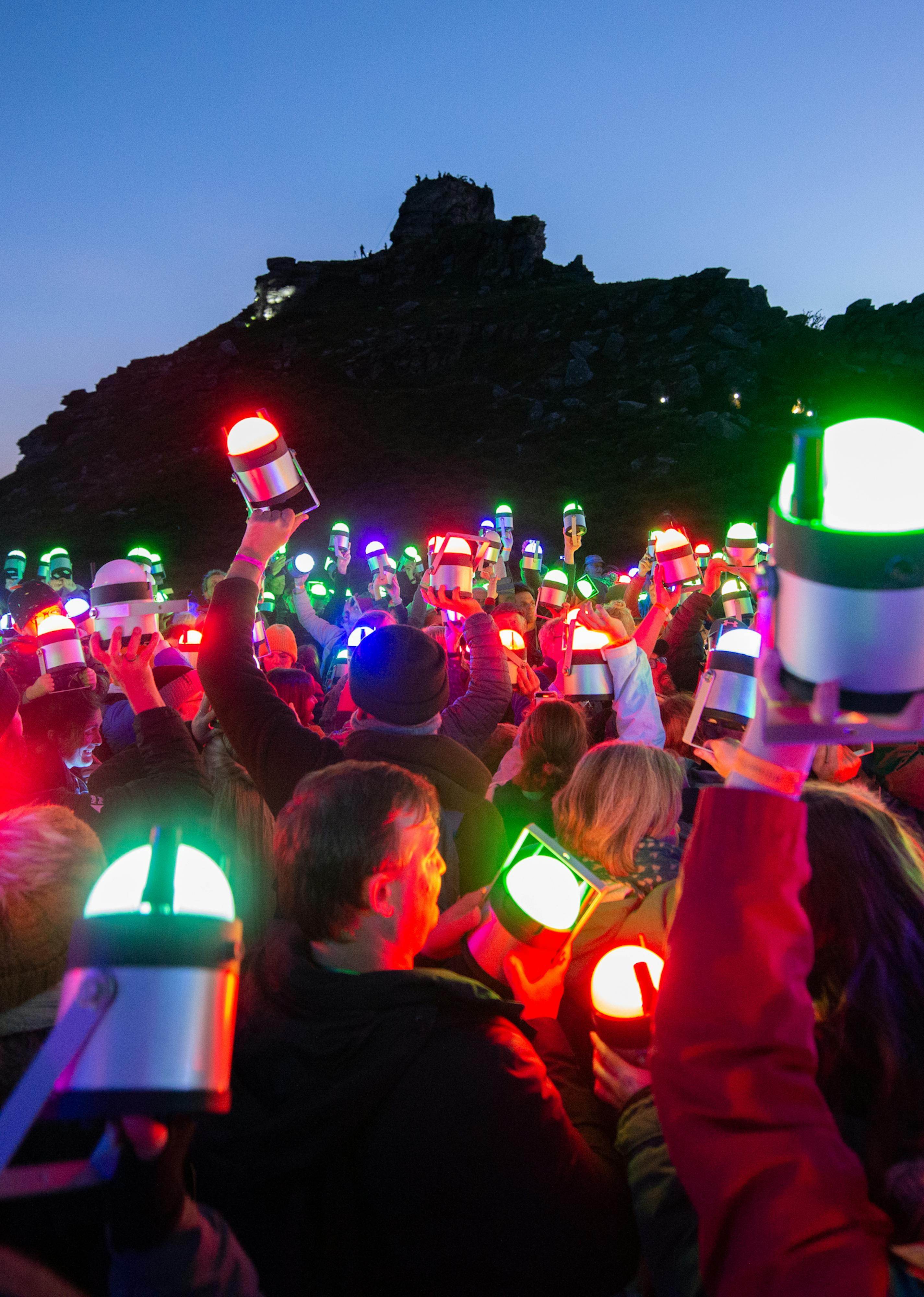 Lumenators holding up their geolights into the sky, lit in different colours as the sun goes down
