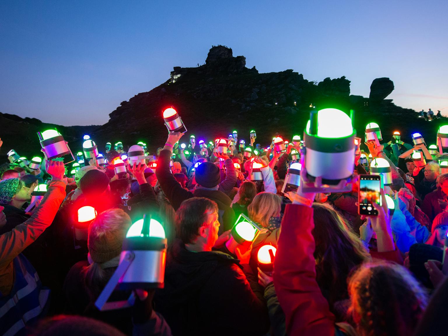 Lumenators holding up their geolights into the sky, lit in different colours as the sun goes down