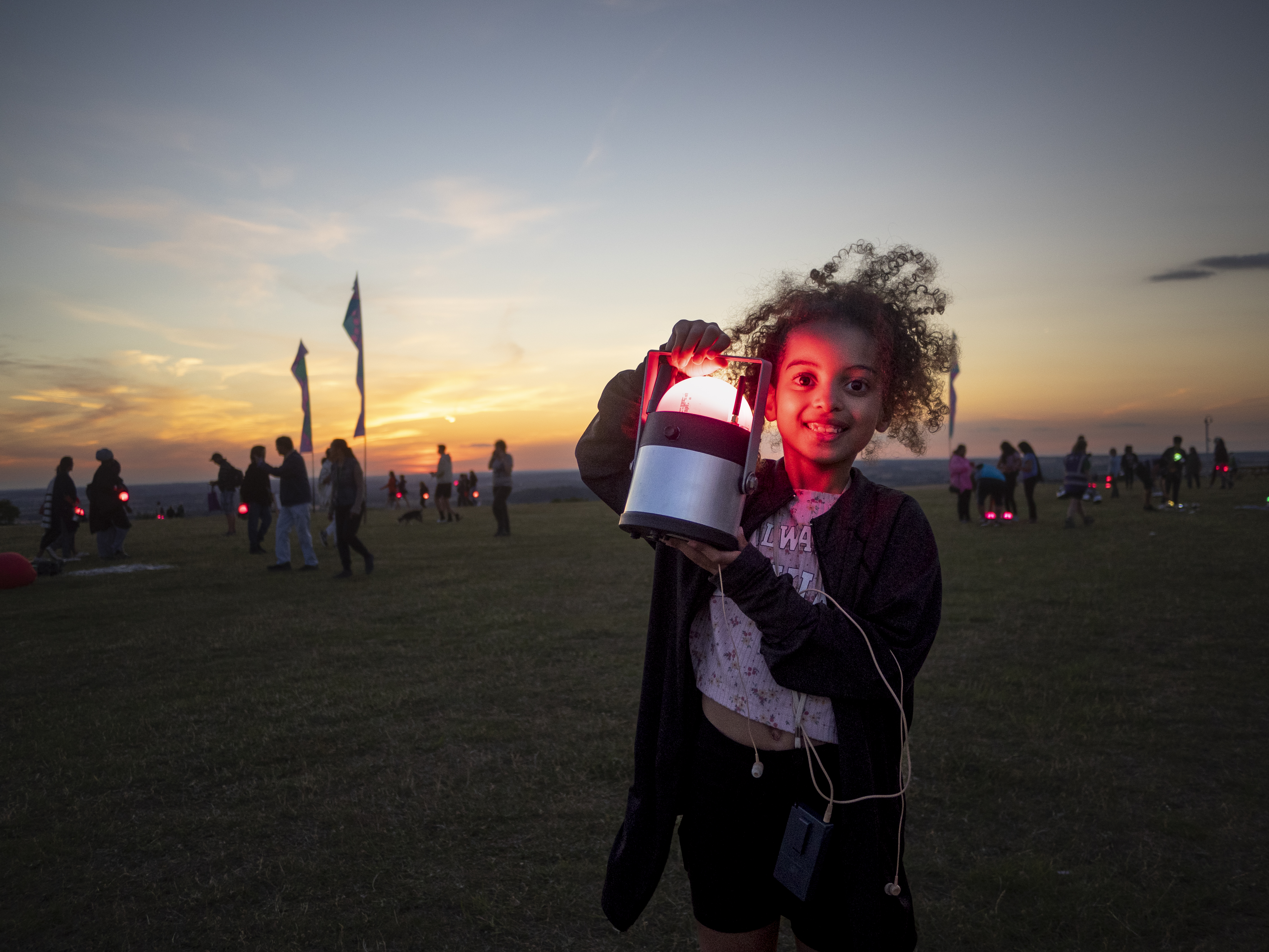 A young girl holding up a Geolight in front of the sunset