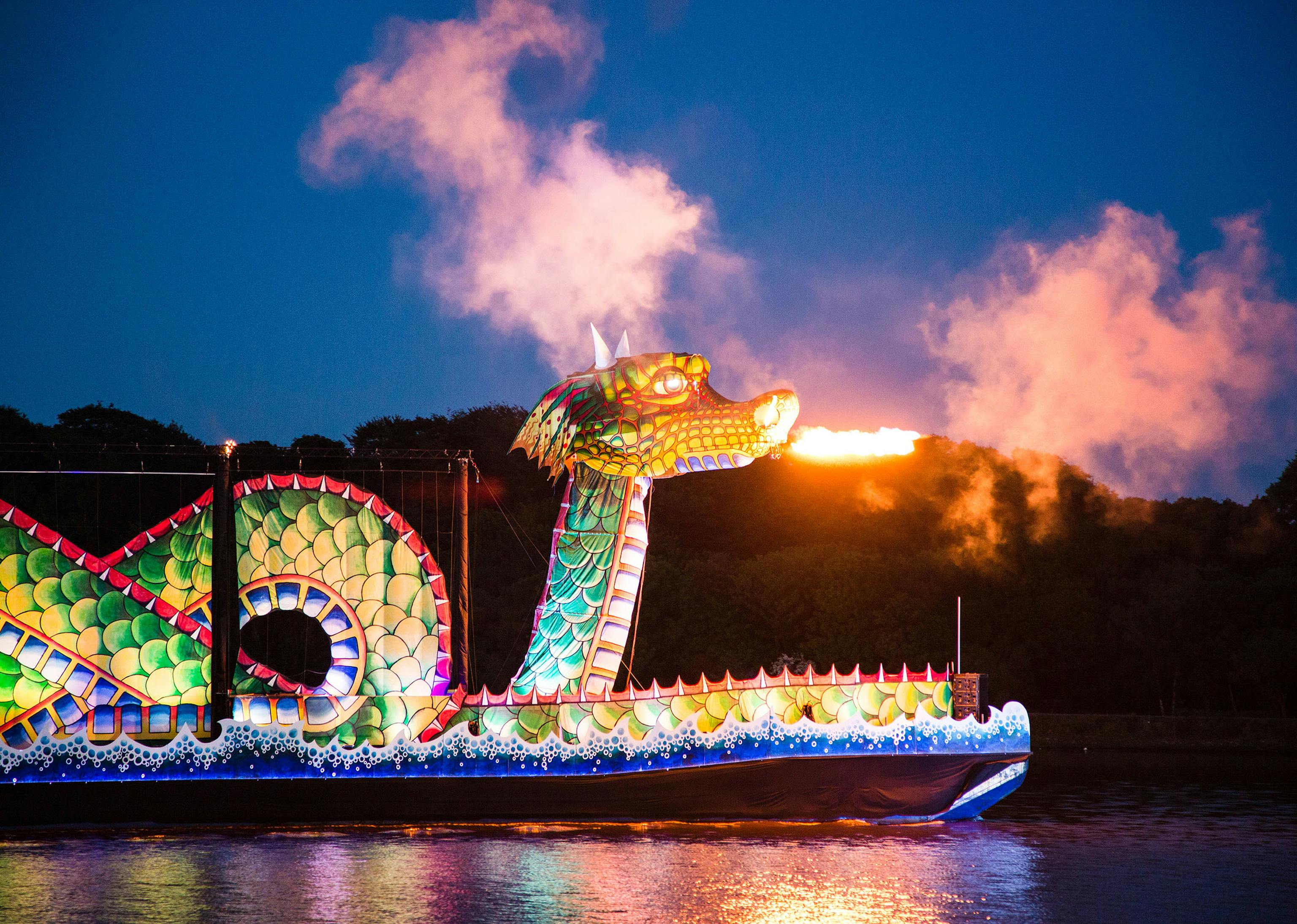 A large green dragon atop a boat breathing fire 