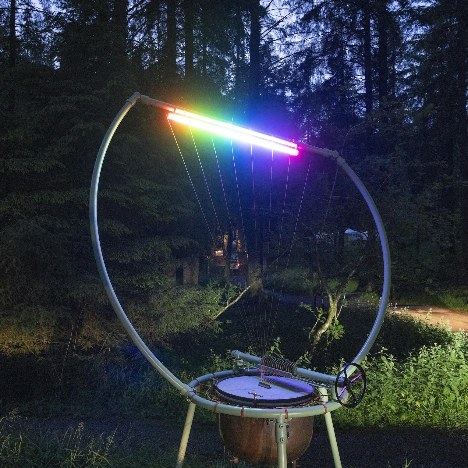A Timpani Harp lit up in a rainbow of lighting in a wood in the dark