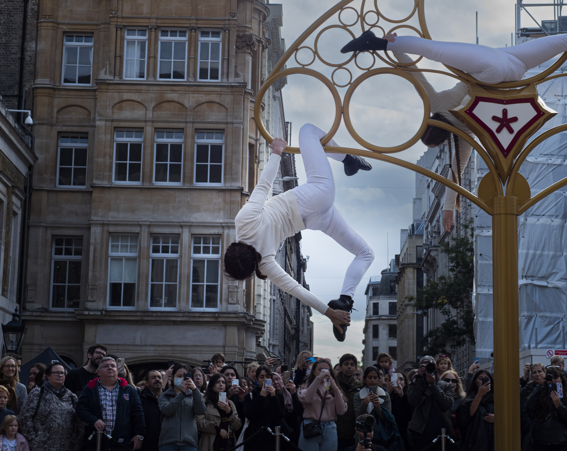 An acrobat wearing all white hangs off the edge of a giant metal key