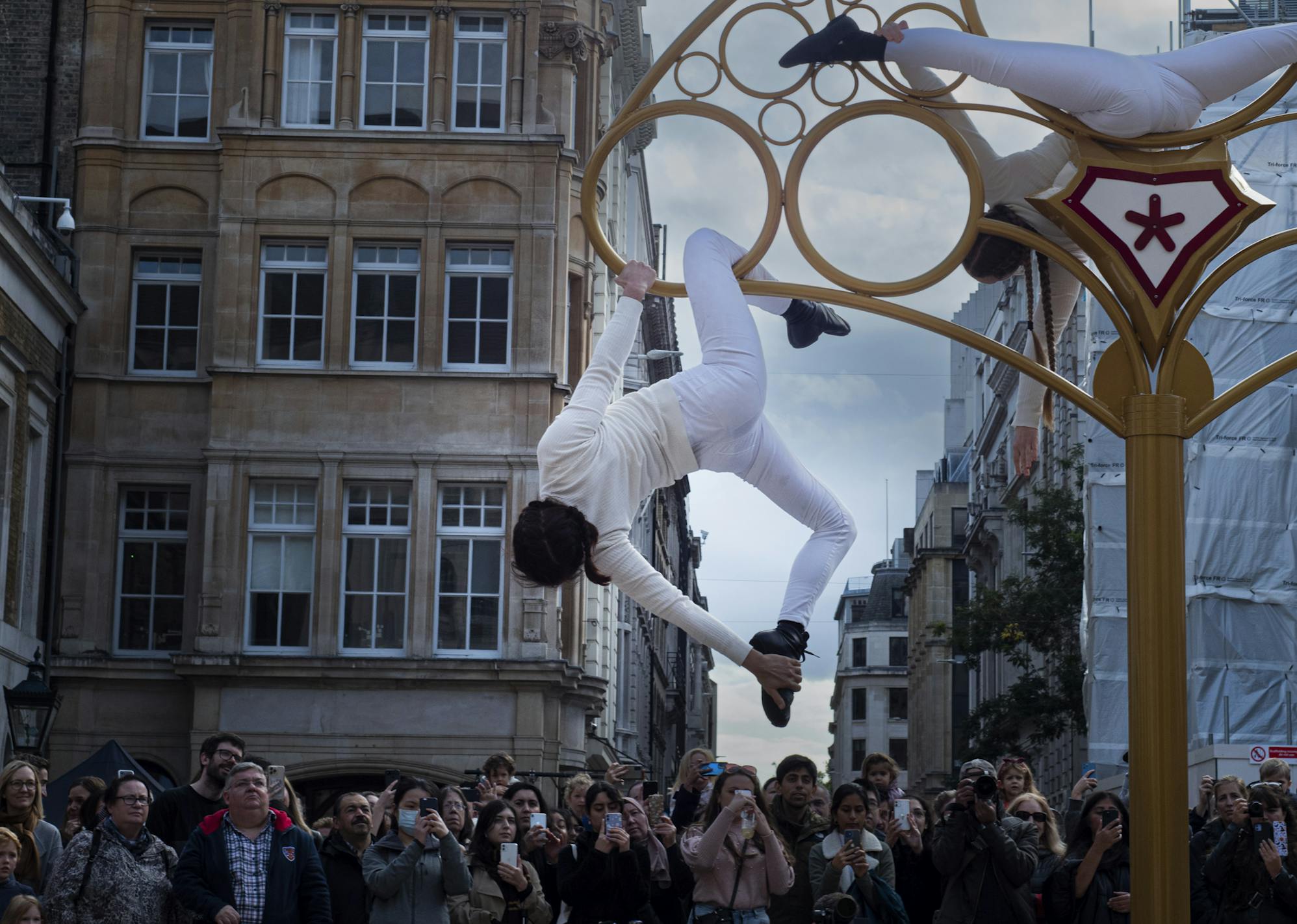 An acrobat wearing all white hangs off the edge of a giant metal key