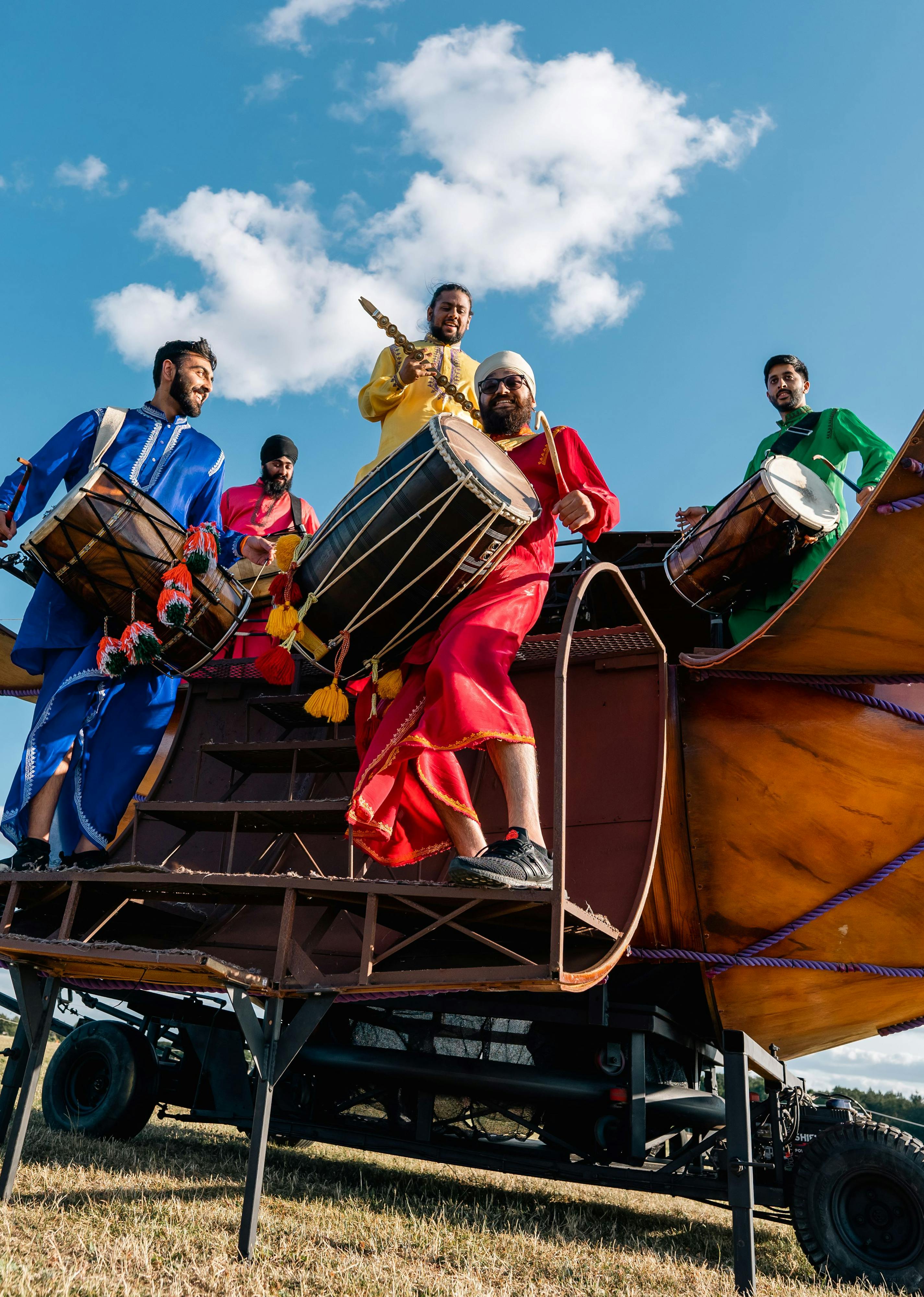 Six drummers in brightly coloured clothing standing inside a giant Dhol Drum