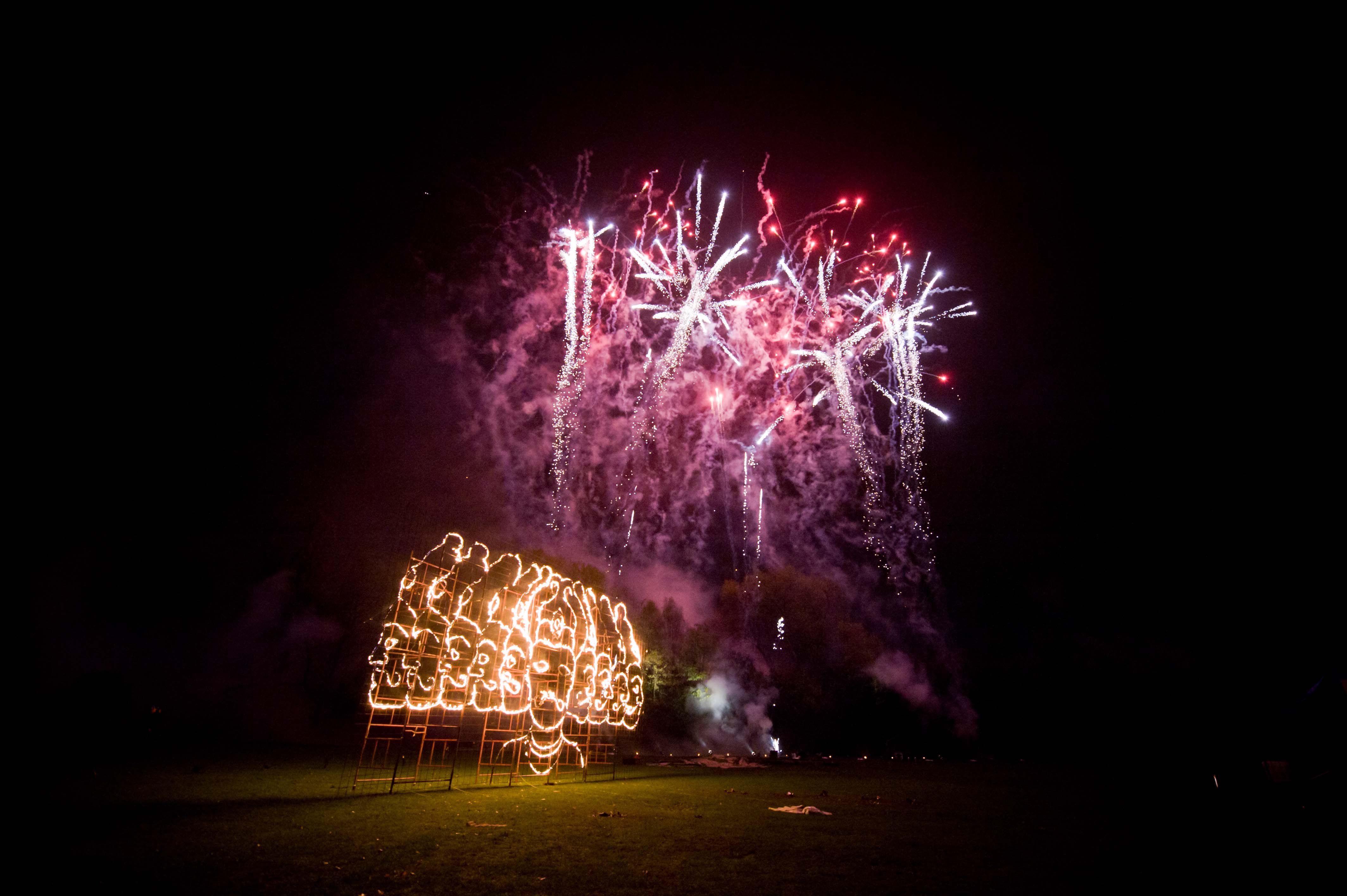 Fireworks above a fire drawing of a multi-headed person