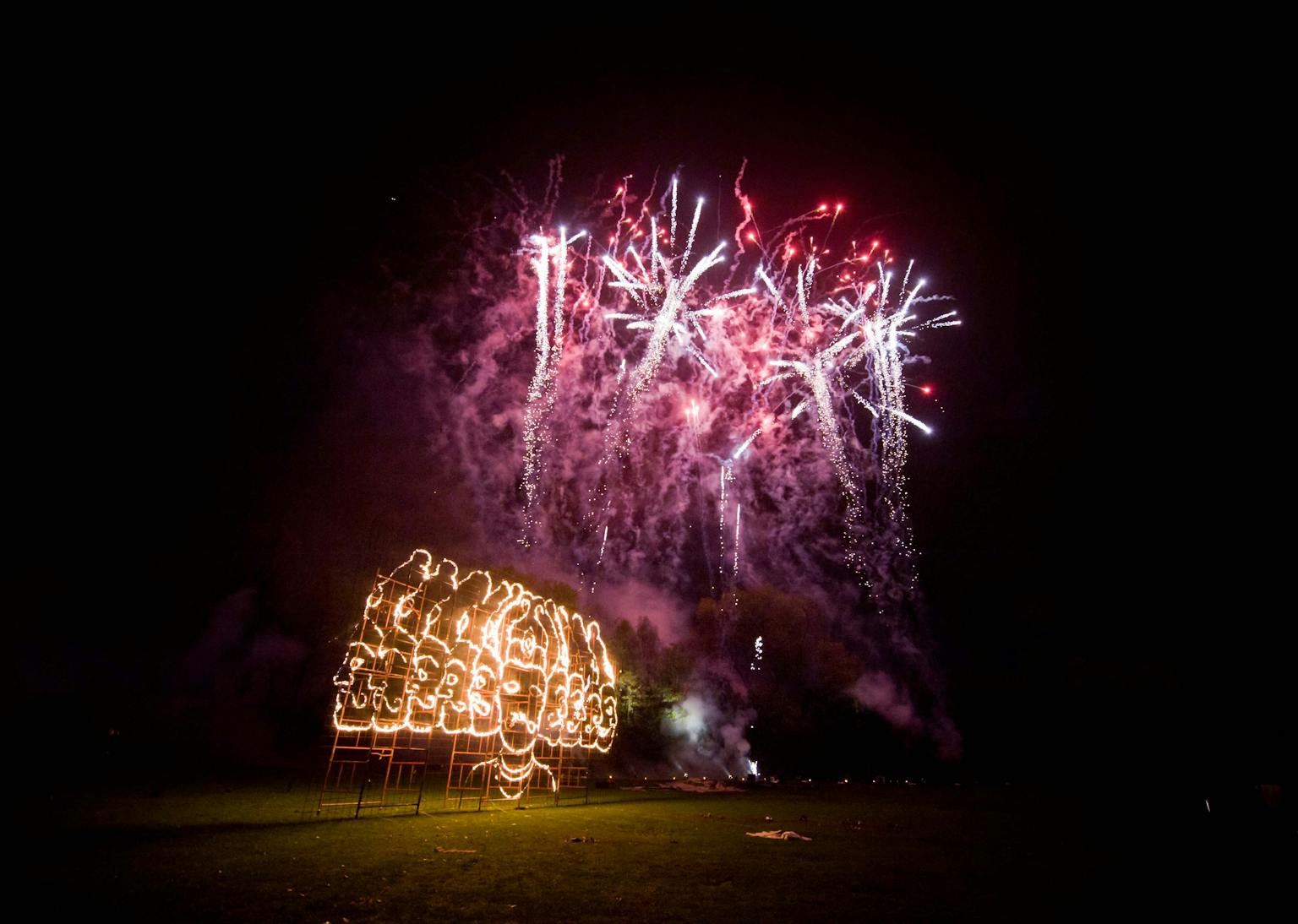 Fireworks above a fire drawing of a multi-headed person