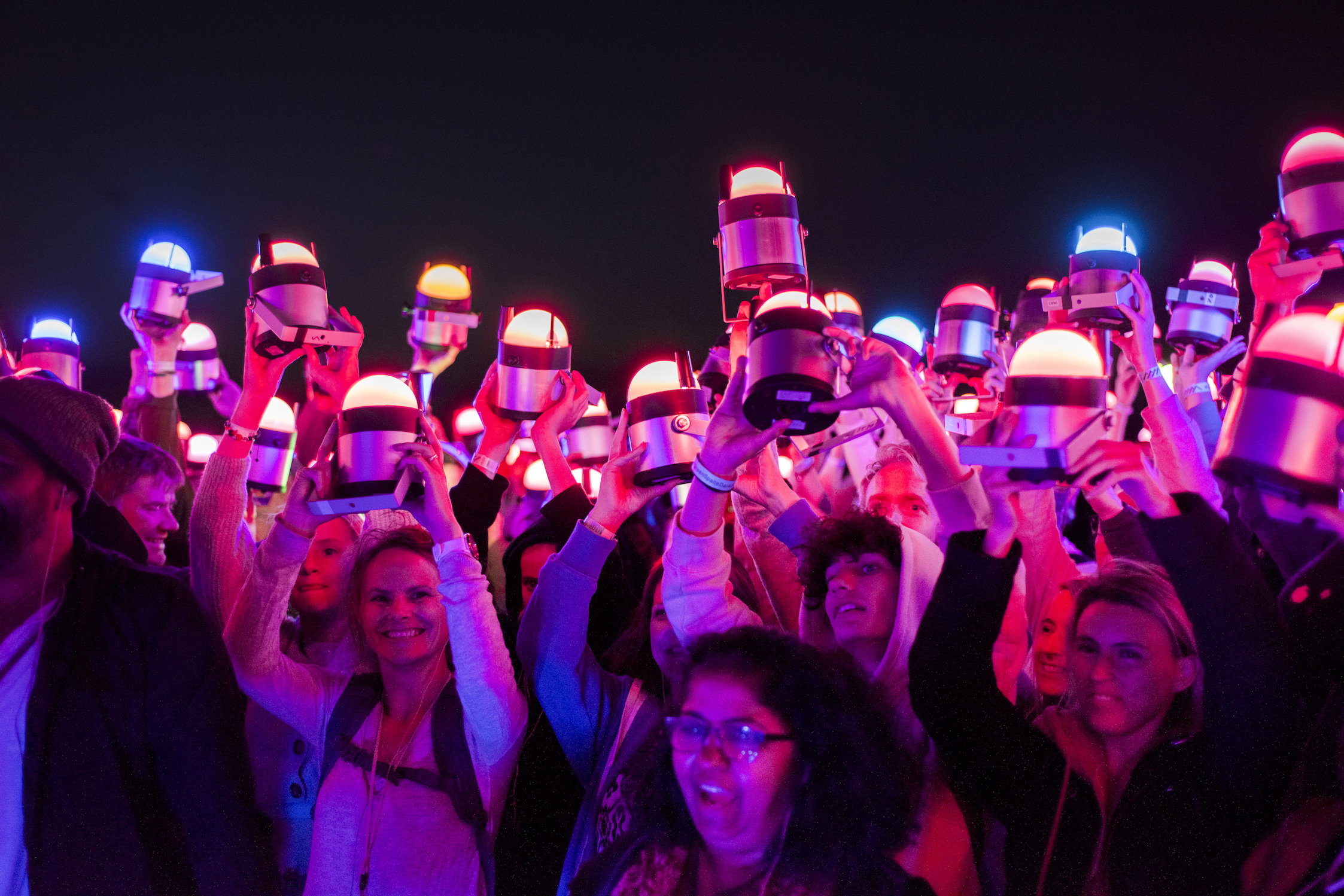 A group of people all holding pink-toned lights above their heads