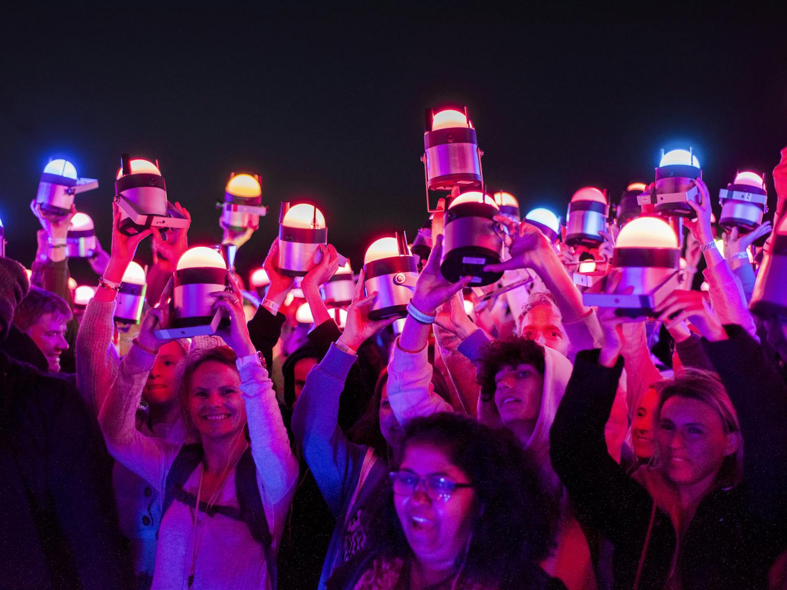 A group of people all holding pink-toned lights above their heads