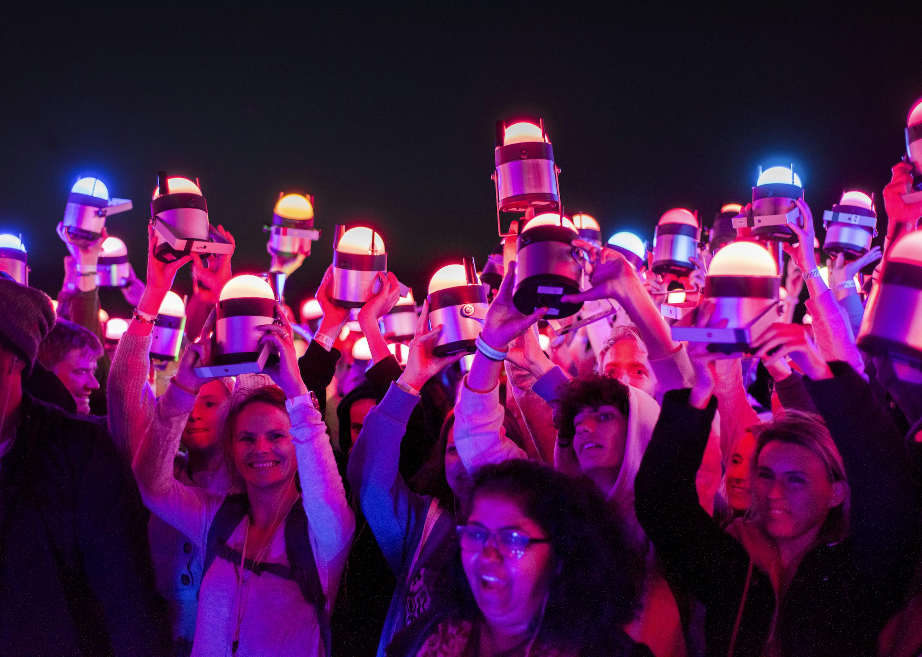A group of people all holding pink-toned lights above their heads