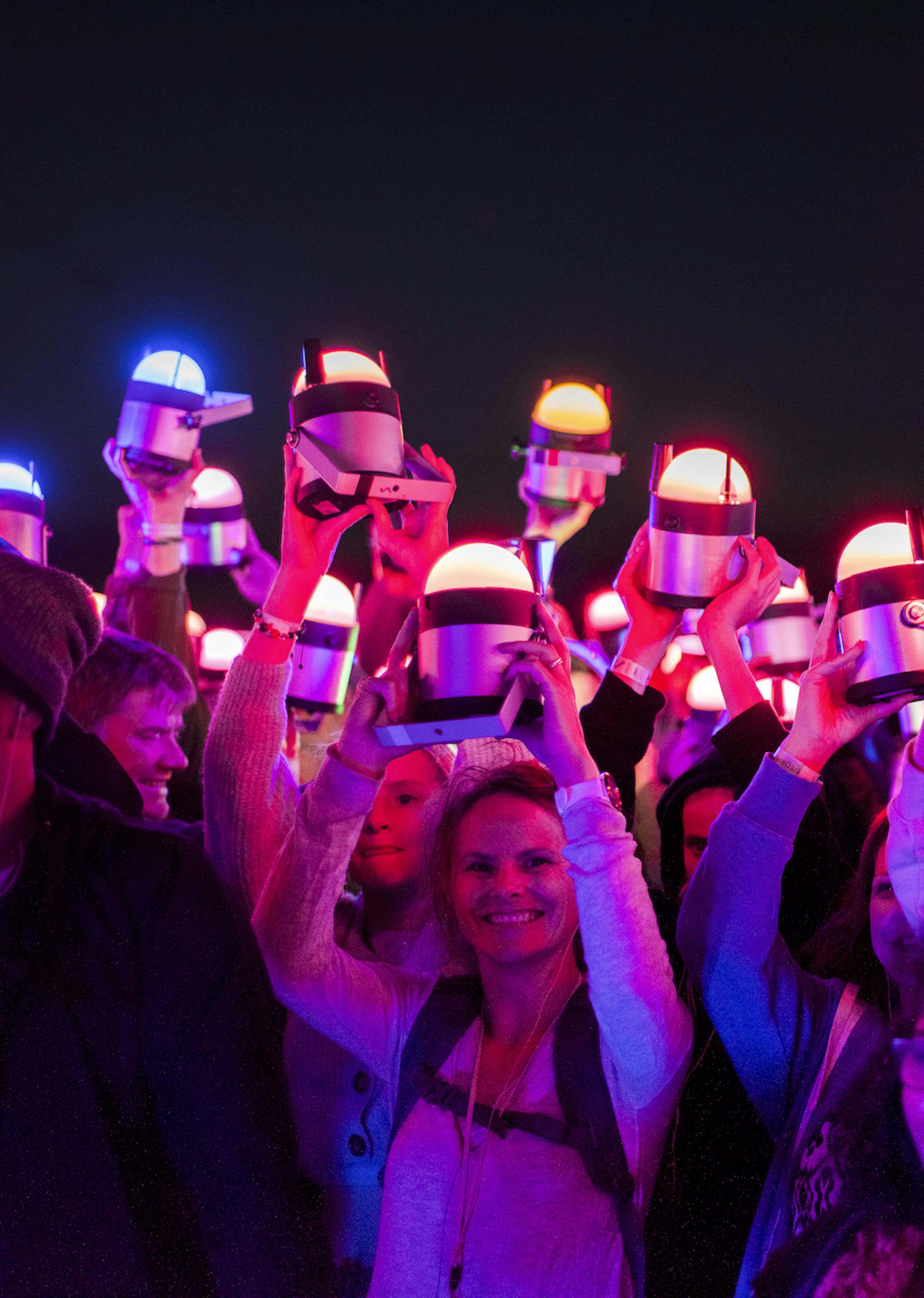 A group of people all holding pink-toned lights above their heads
