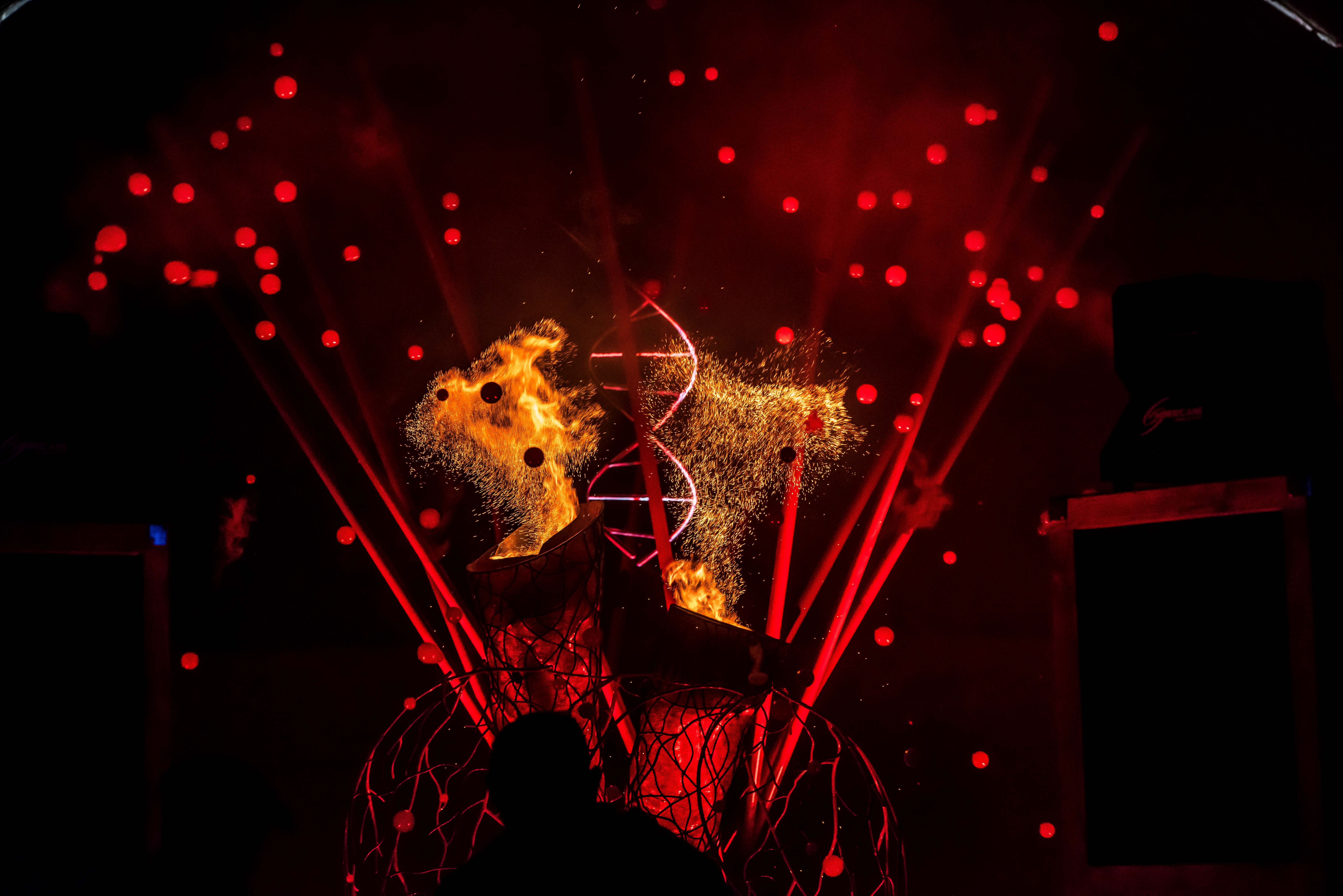 A structure of an organ heart lit in red with pyro and glowing red bubbles in the background. 