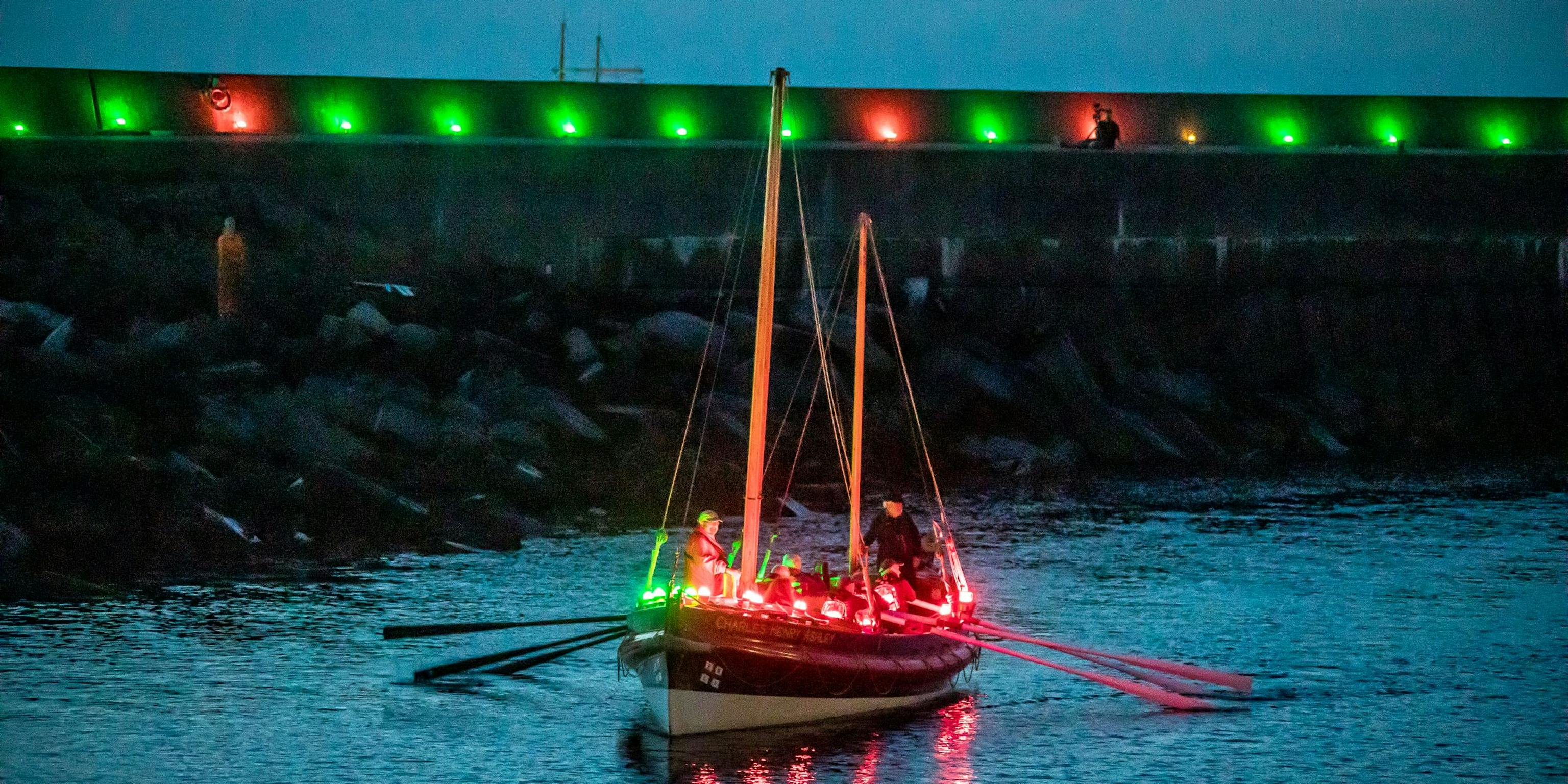 A boat filled with Red and Green Geolights leaving a harbour that is also lined in Geolights