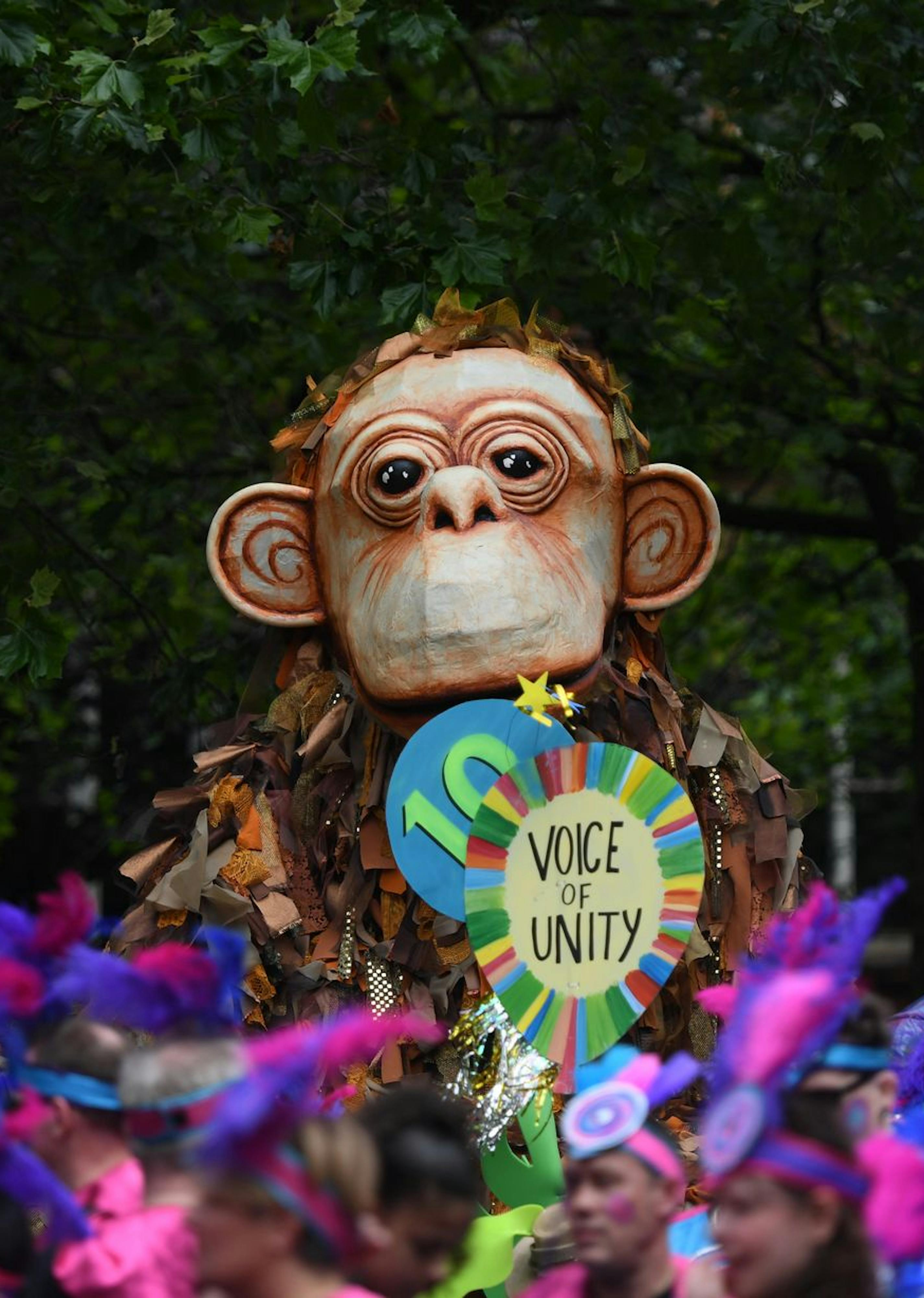 A giant puppet monkey with a paper mache face and a calico body in a crowded parade.