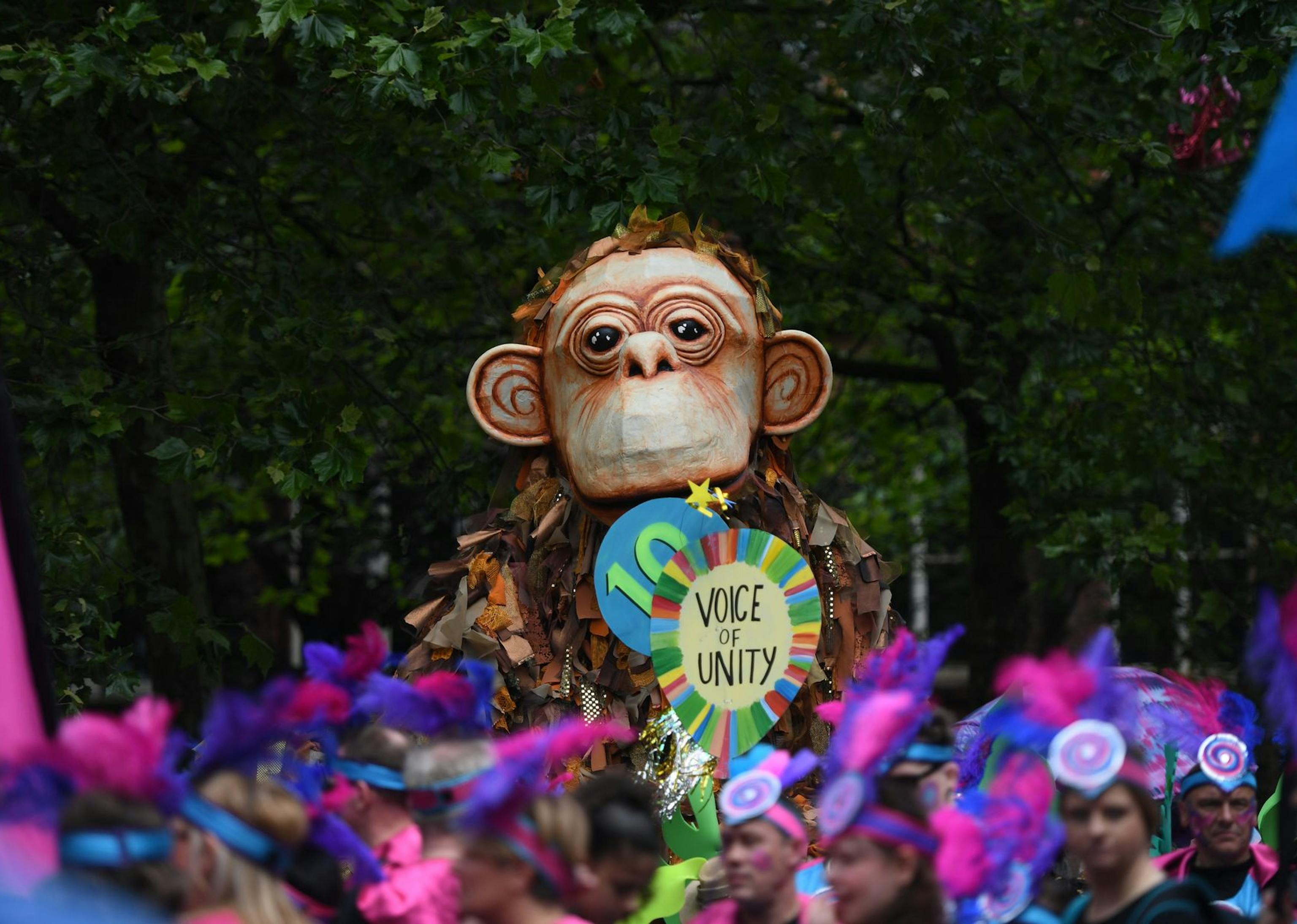 A giant puppet monkey with a paper mache face and a calico body in a crowded parade.