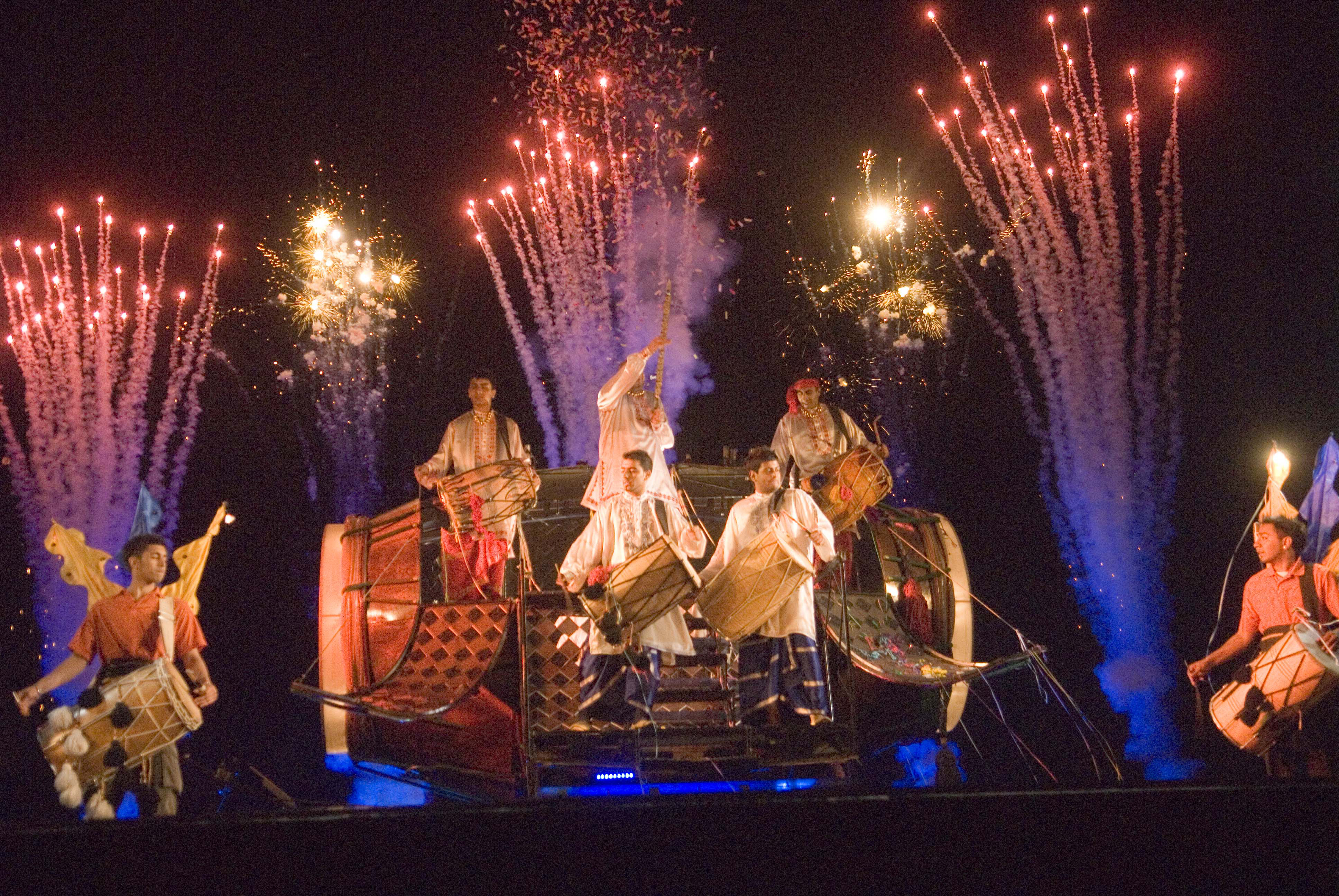 Drummers inside a giant Dhol drum with fireworks going off behind them