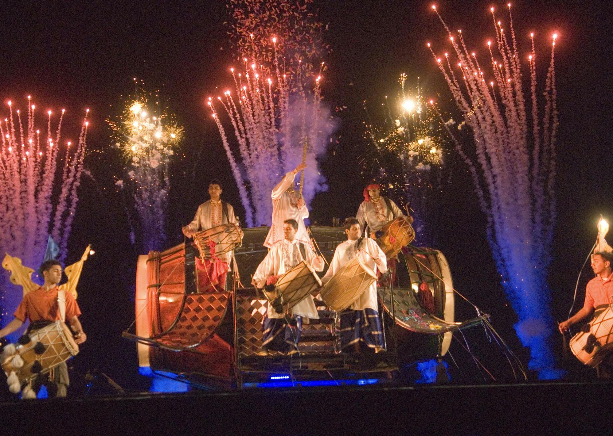 Drummers inside a giant Dhol drum with fireworks going off behind them