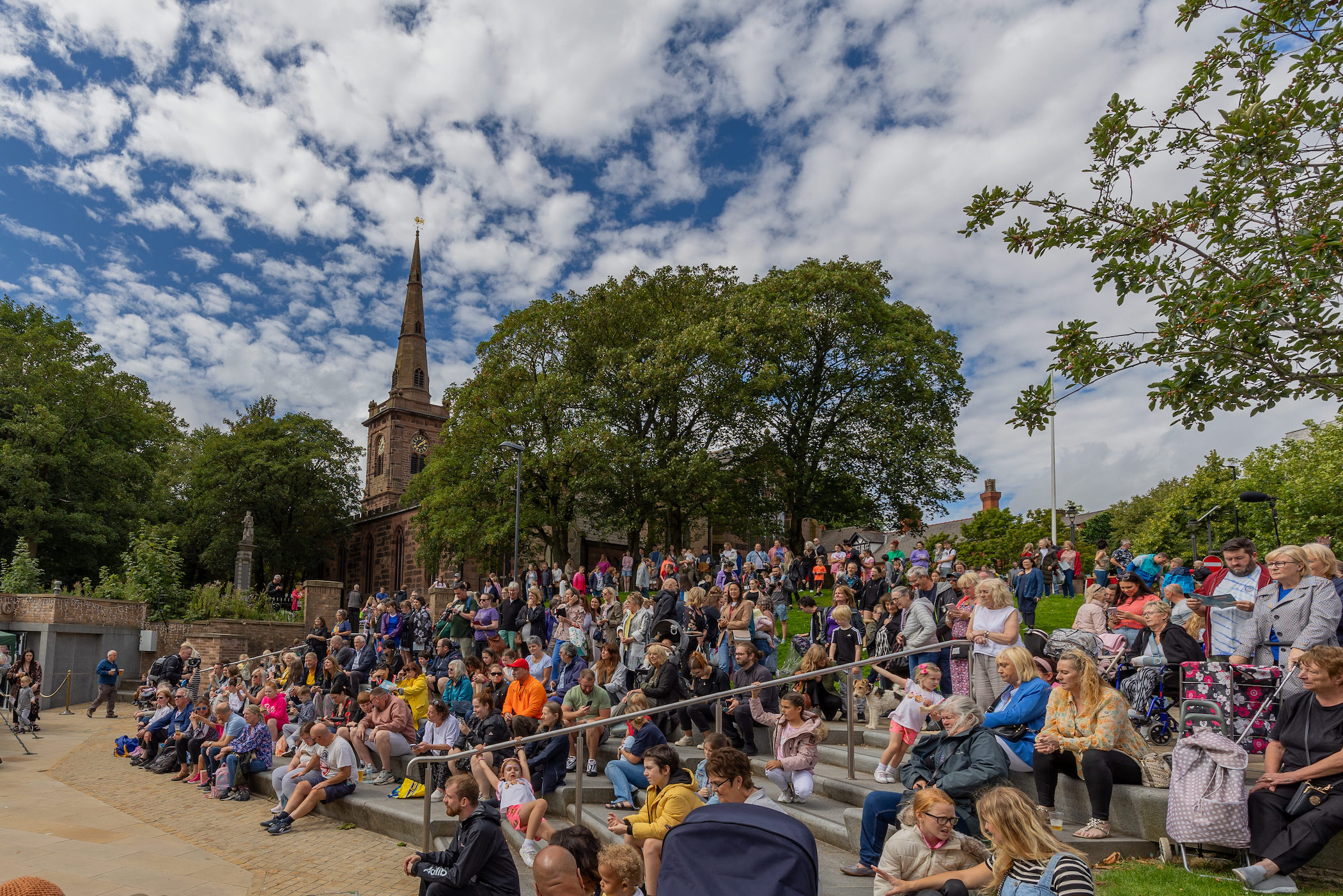 A crowd of people sitting on steps watching a performance with cloudy skies over head