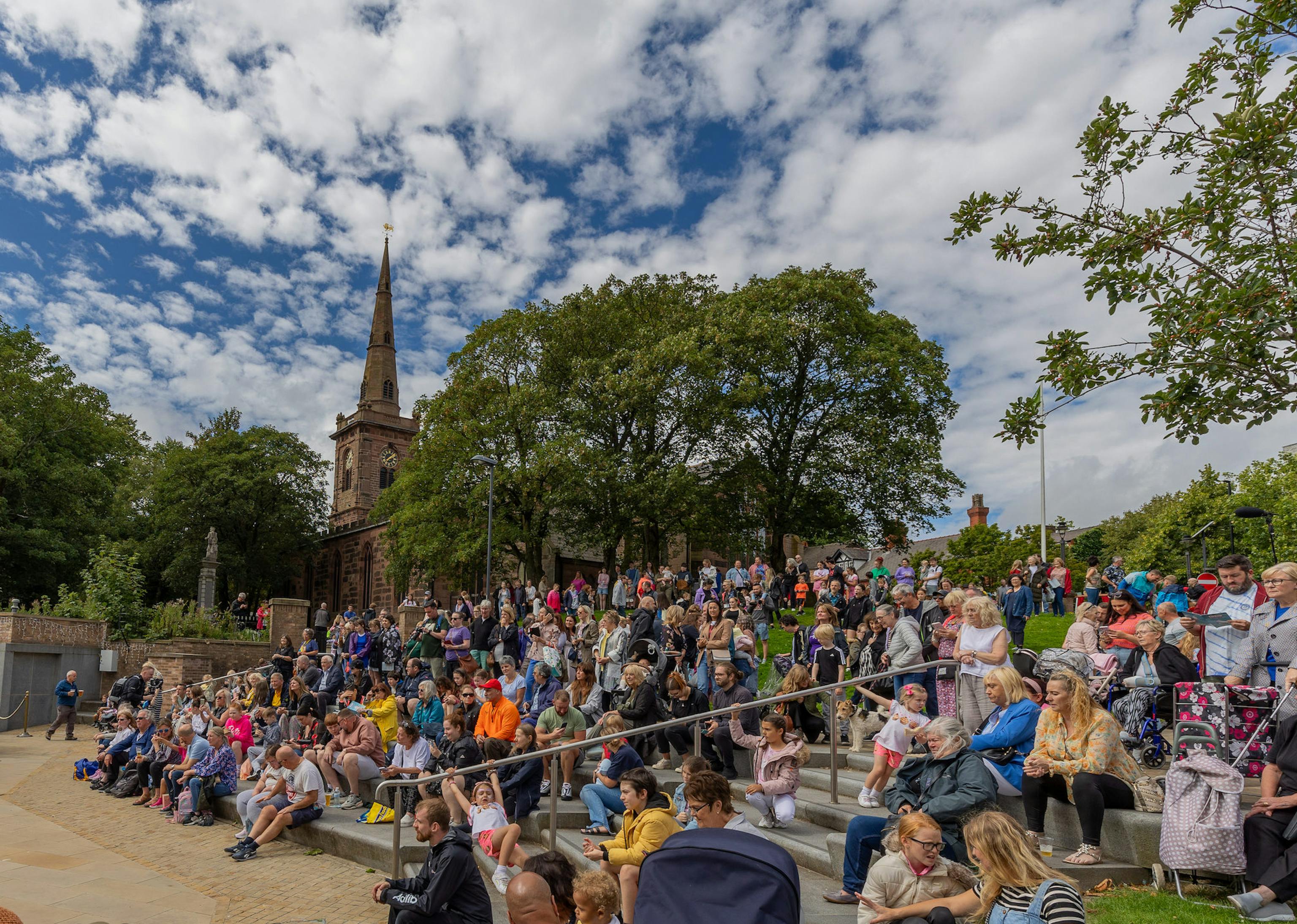 A crowd of people sitting on steps watching a performance with cloudy skies over head