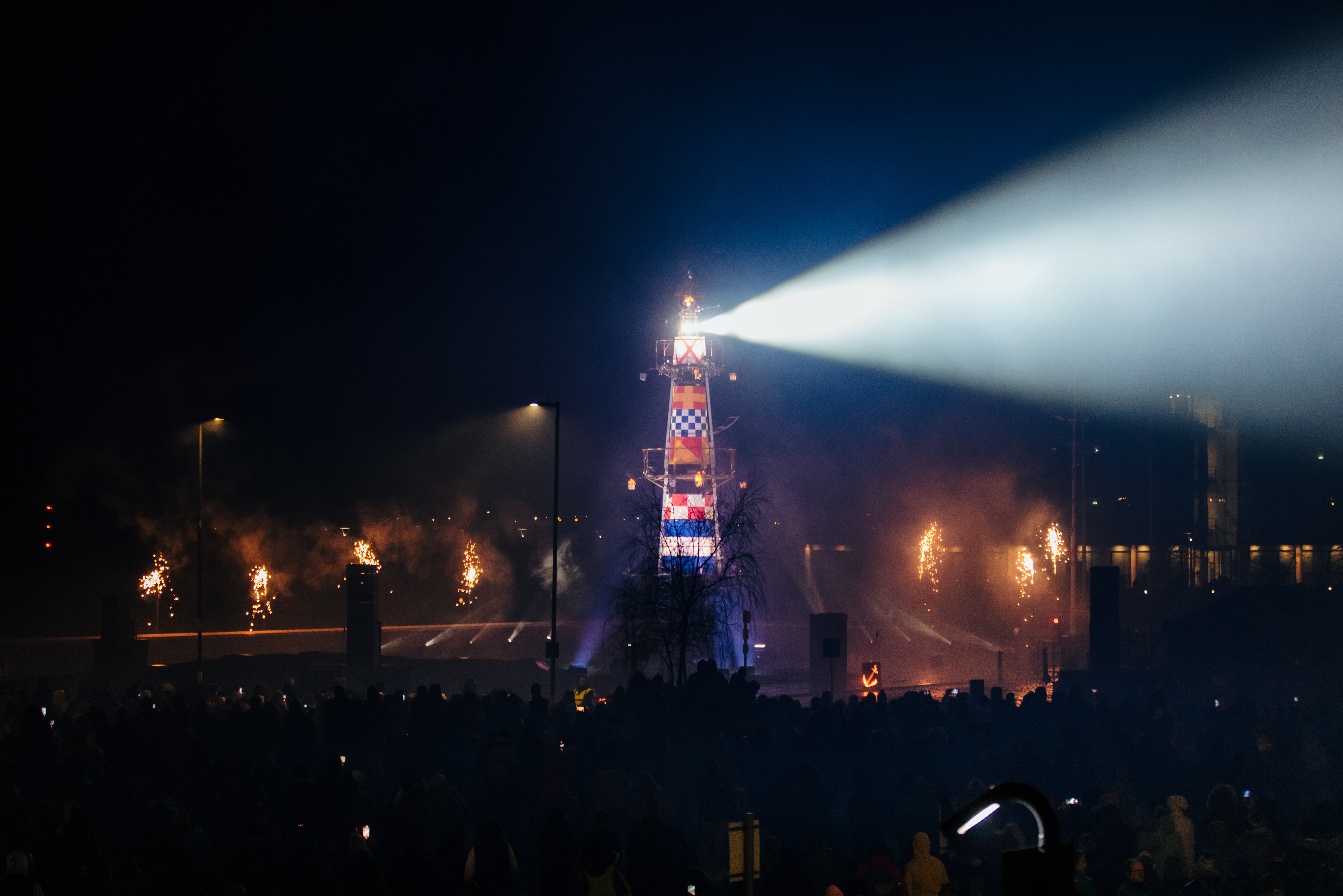 A lighthouse structure at night, with a light beaming out at an audience of thousands, at night. 