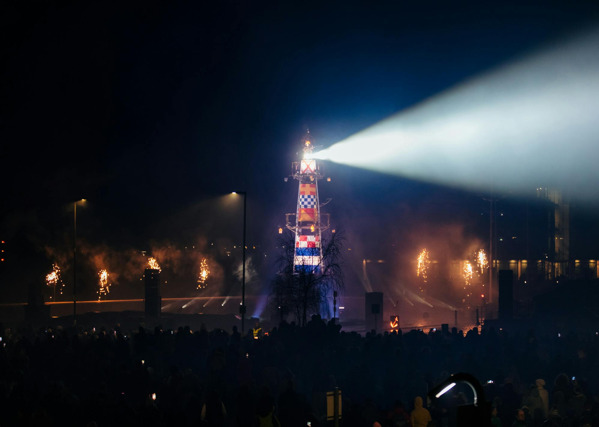 A lighthouse structure at night, with a light beaming out at an audience of thousands, at night. 