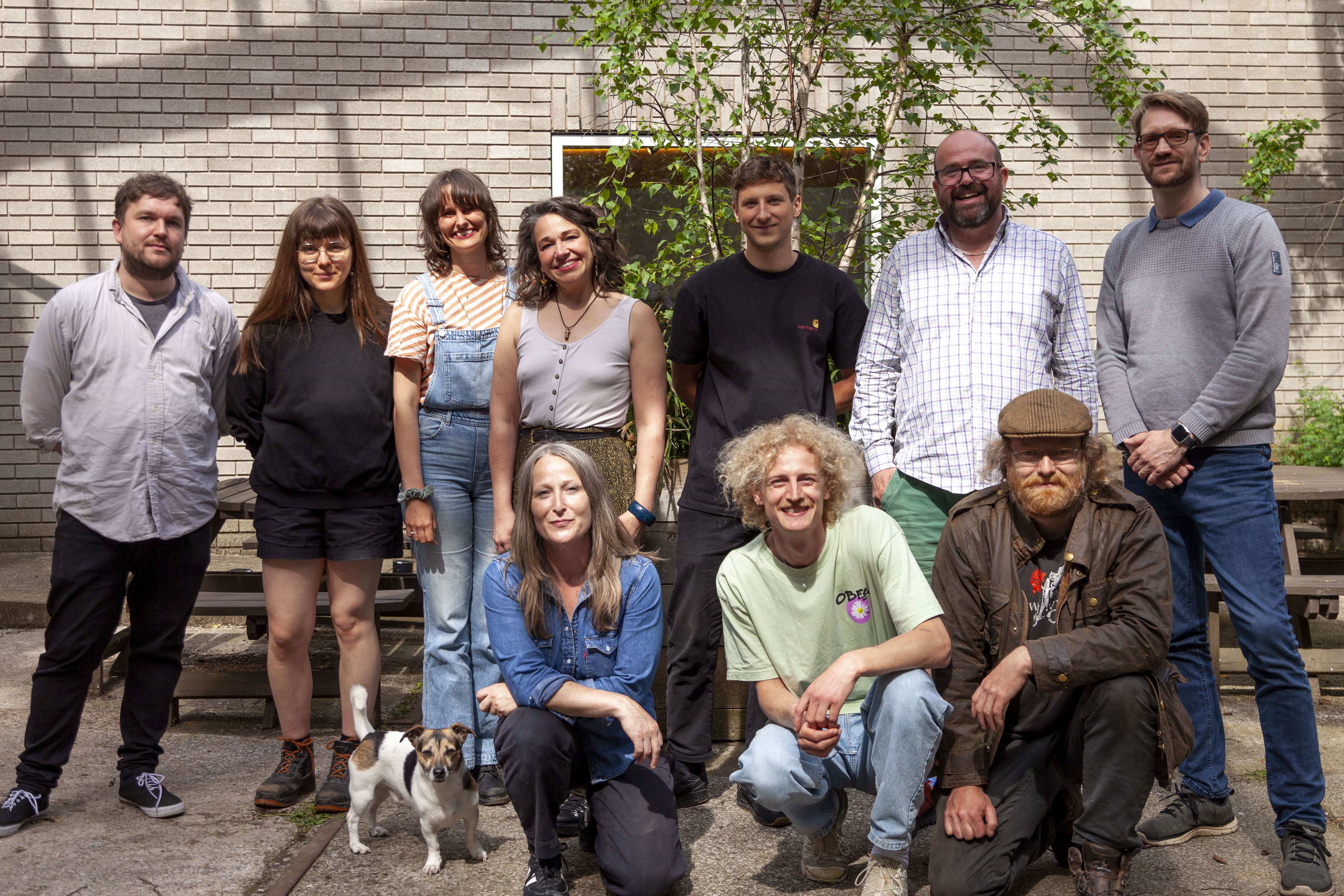 A group of 10 people and 1 dog posing in a sunlit courtyard