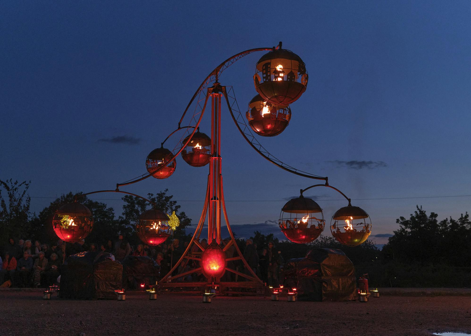 A metal structure balancing a series of globes each with fire inside against a dark sky