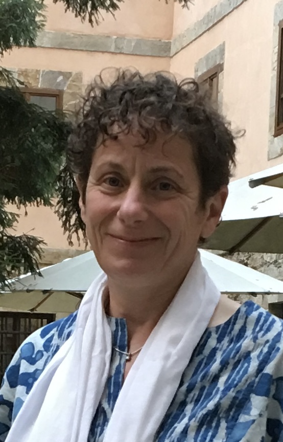 A person with short curly hair, a white scarf and a blue patterned top