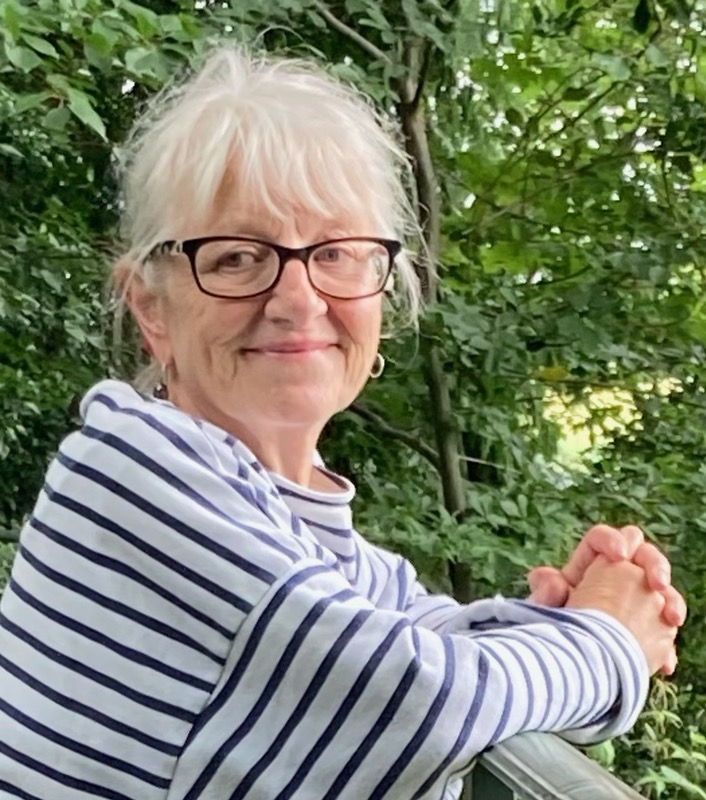 A woman with short white hair and glasses smiles at the camera.