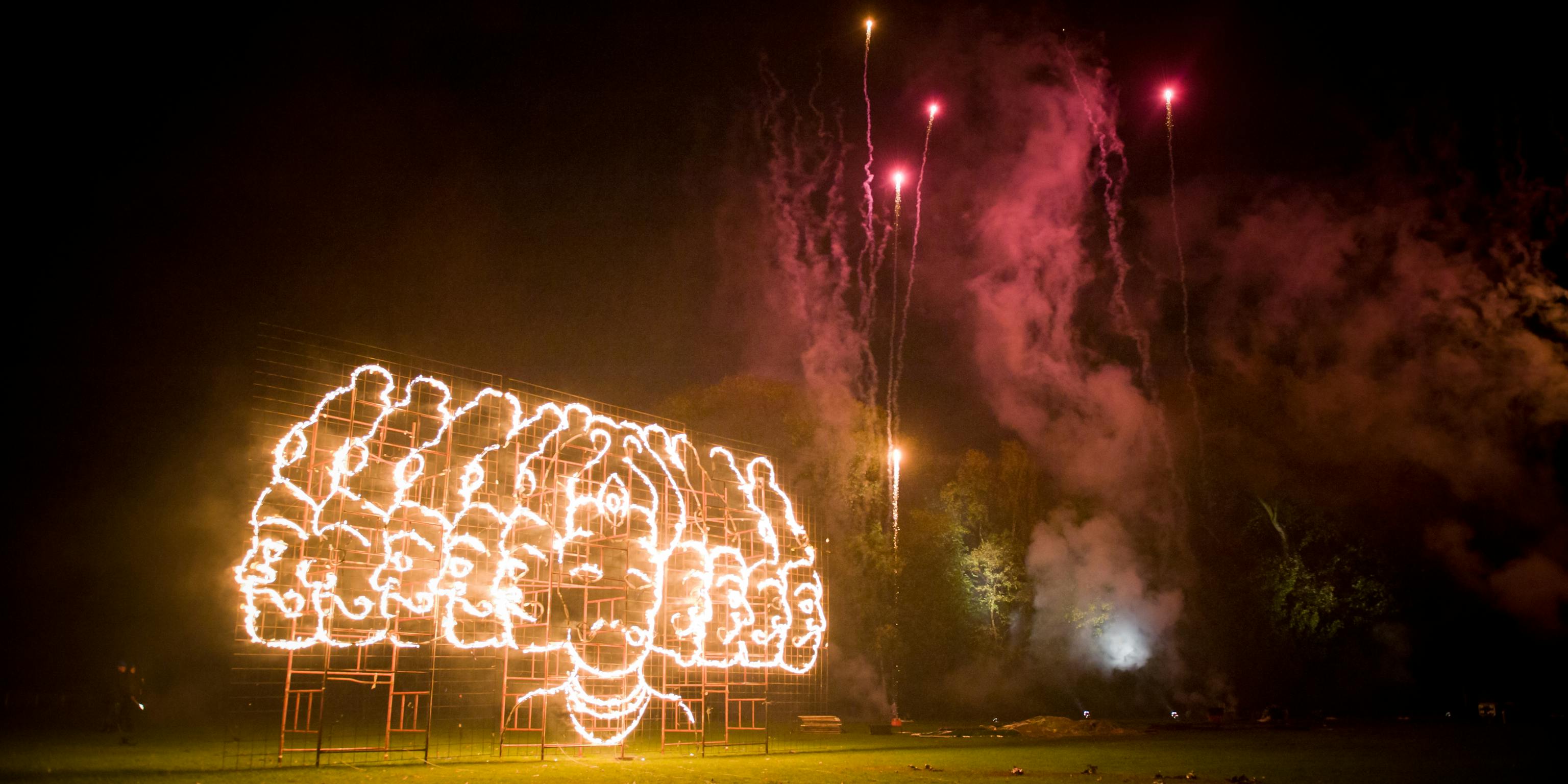 Fireworks above a fire drawing of a multi-headed person