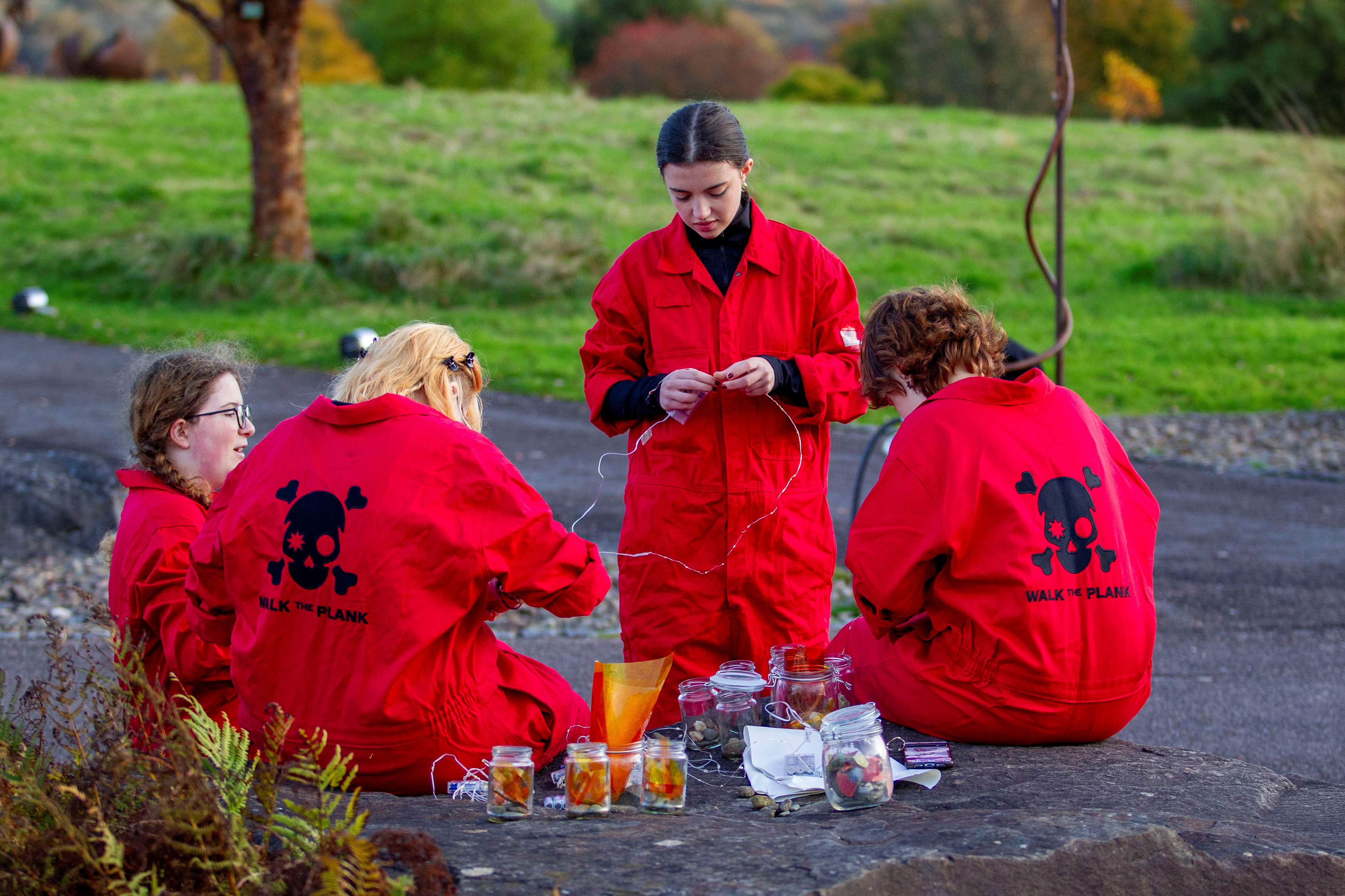 Four people in red overalls sitting and wiring in a green area