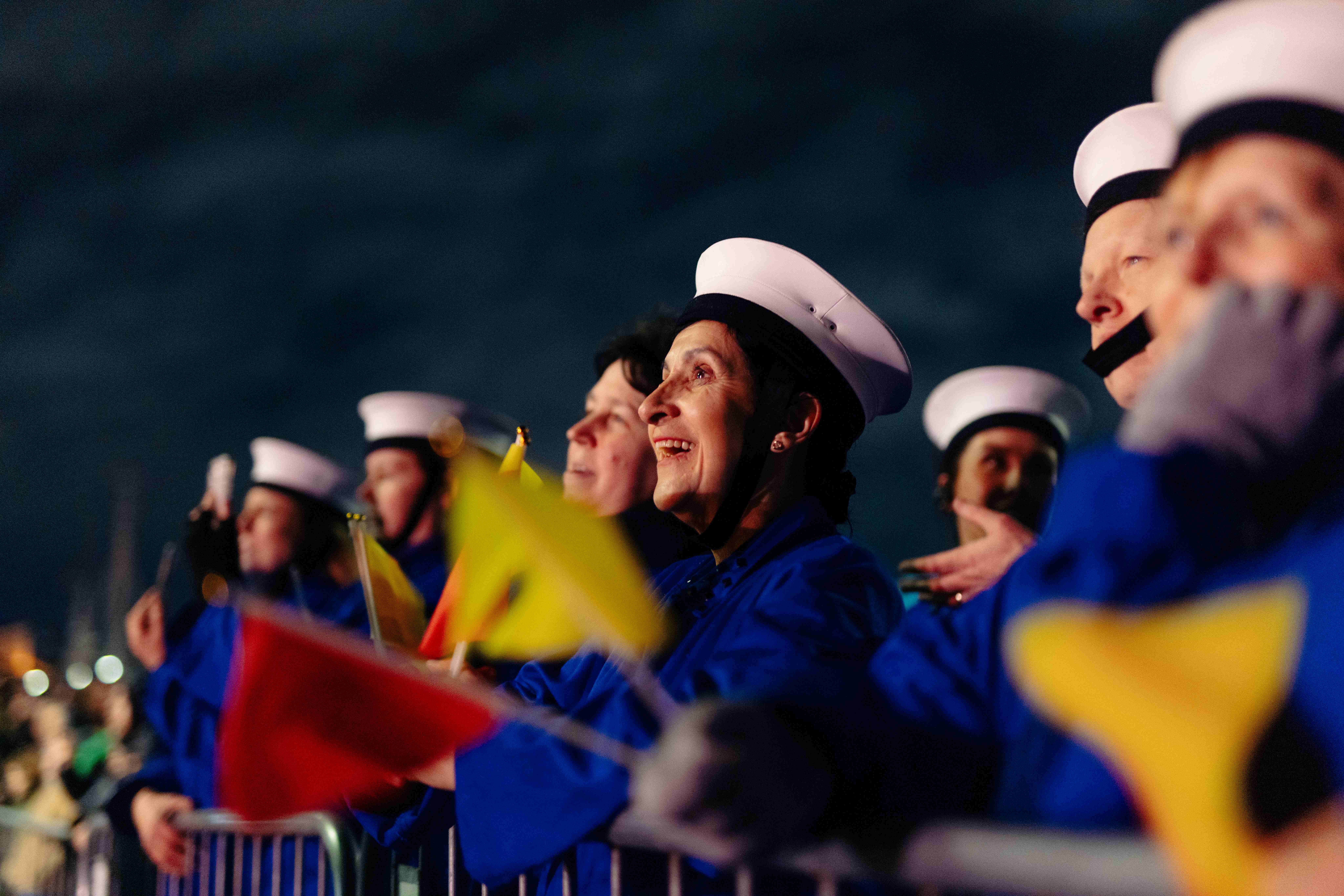 A semaphore team dressed in blue overalls and white hats holding red and yellow flags, smiling.