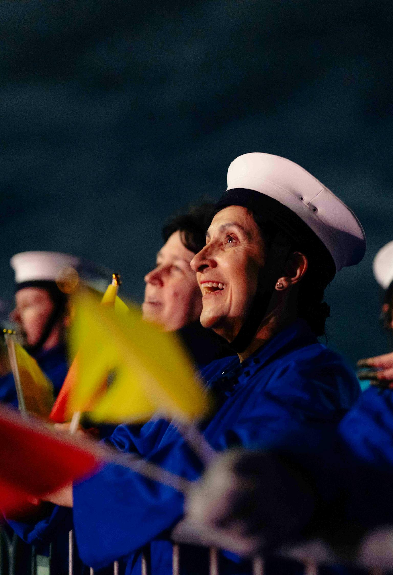 A semaphore team dressed in blue overalls and white hats holding red and yellow flags, smiling.
