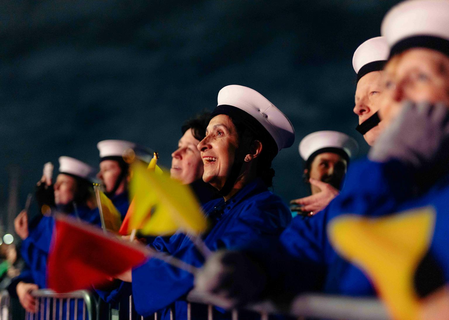 A semaphore team dressed in blue overalls and white hats holding red and yellow flags, smiling.