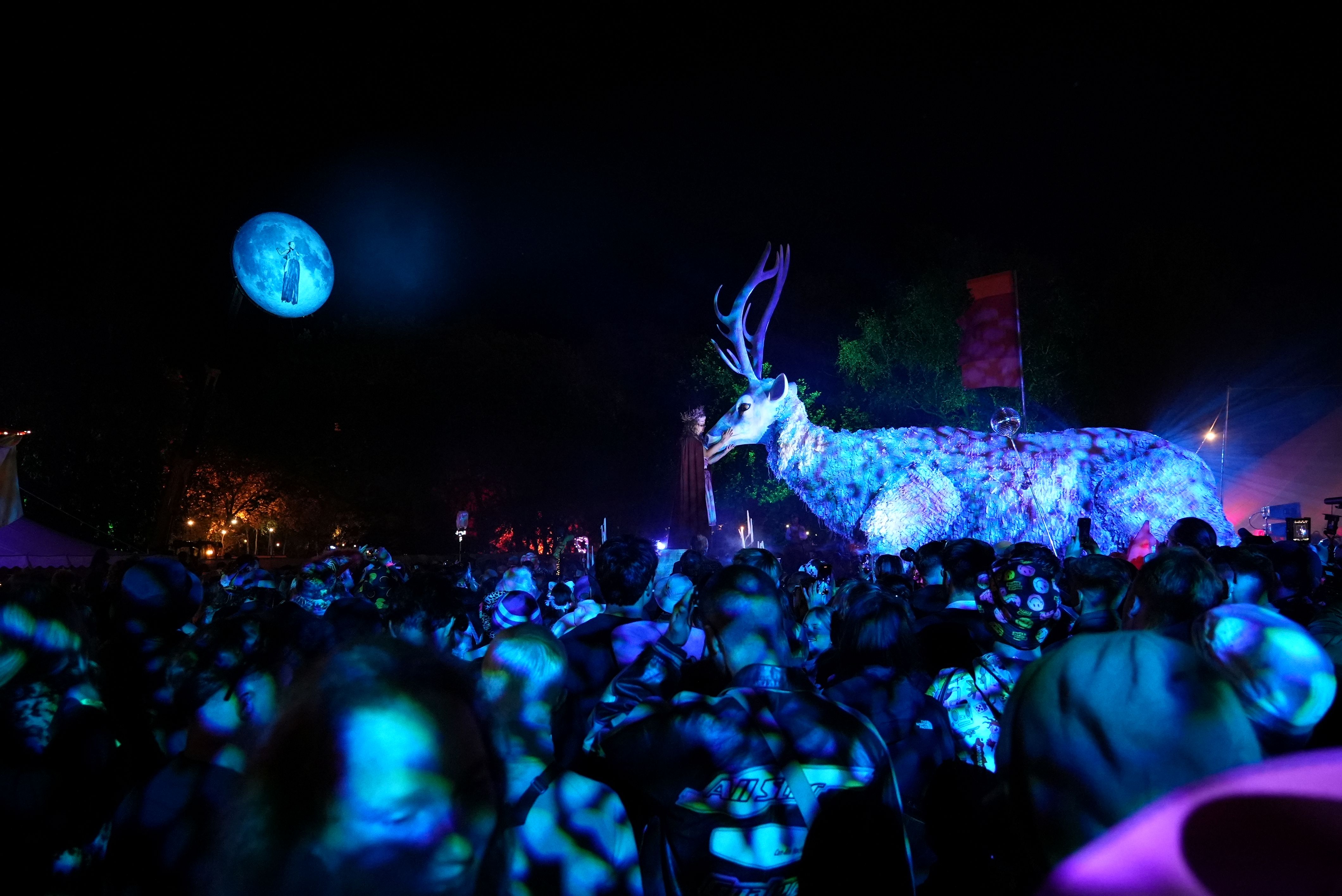 A large puppet of a stag lit with blue light standing amongst a crowd