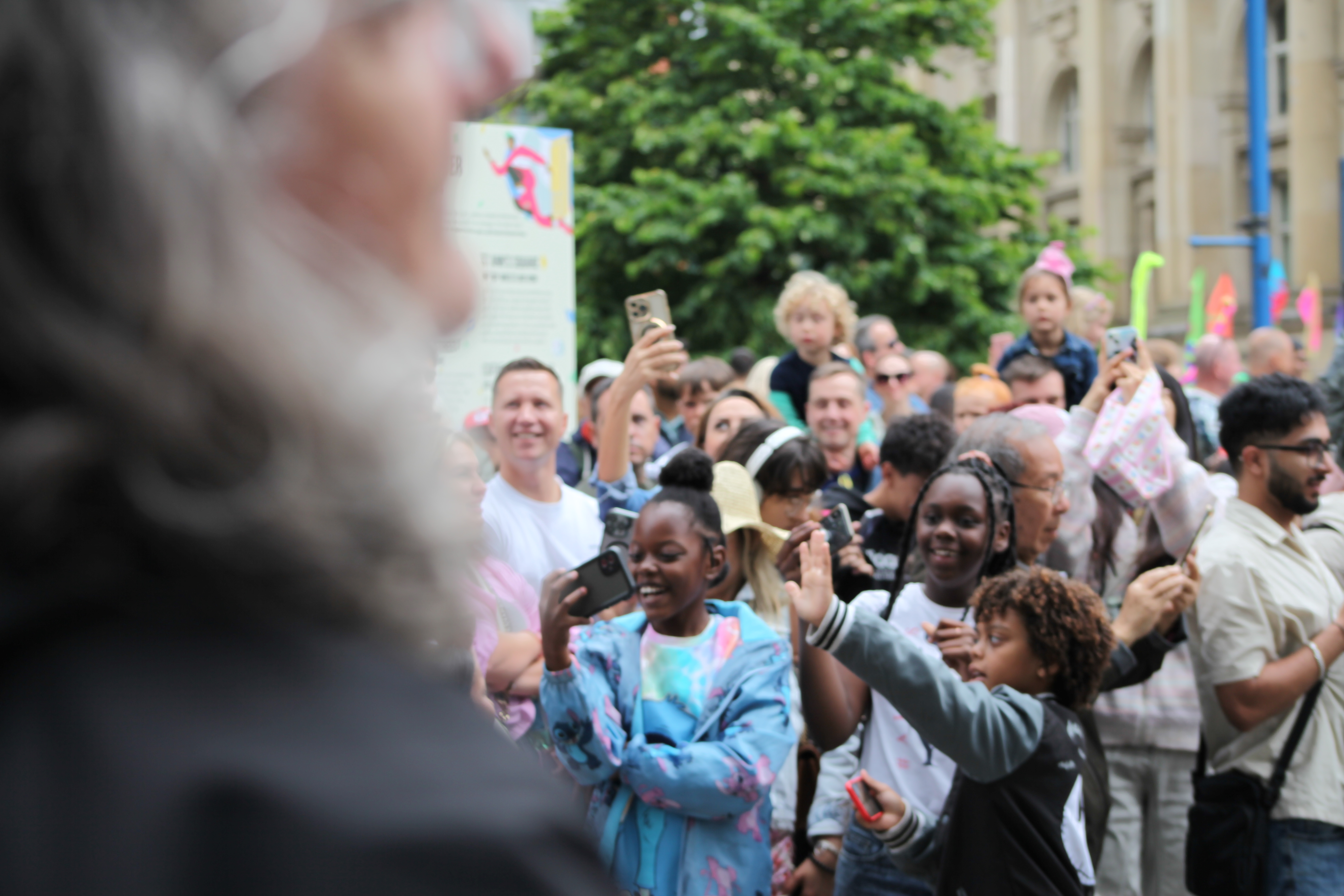 A group of people of all ages joying and taking photos with their phones of a outdoor performance.