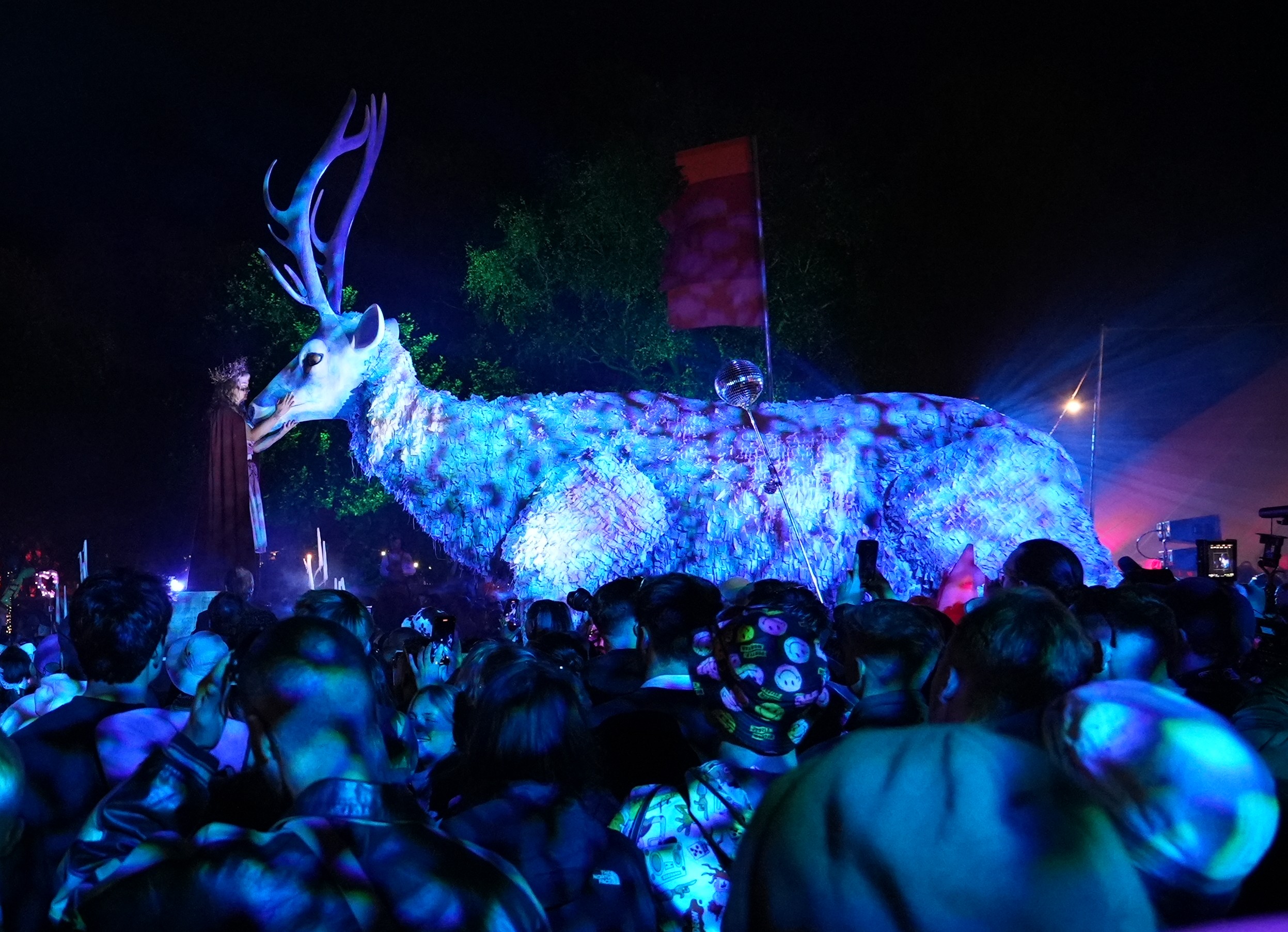 A large puppet of a stag lit with blue light standing amongst a crowd