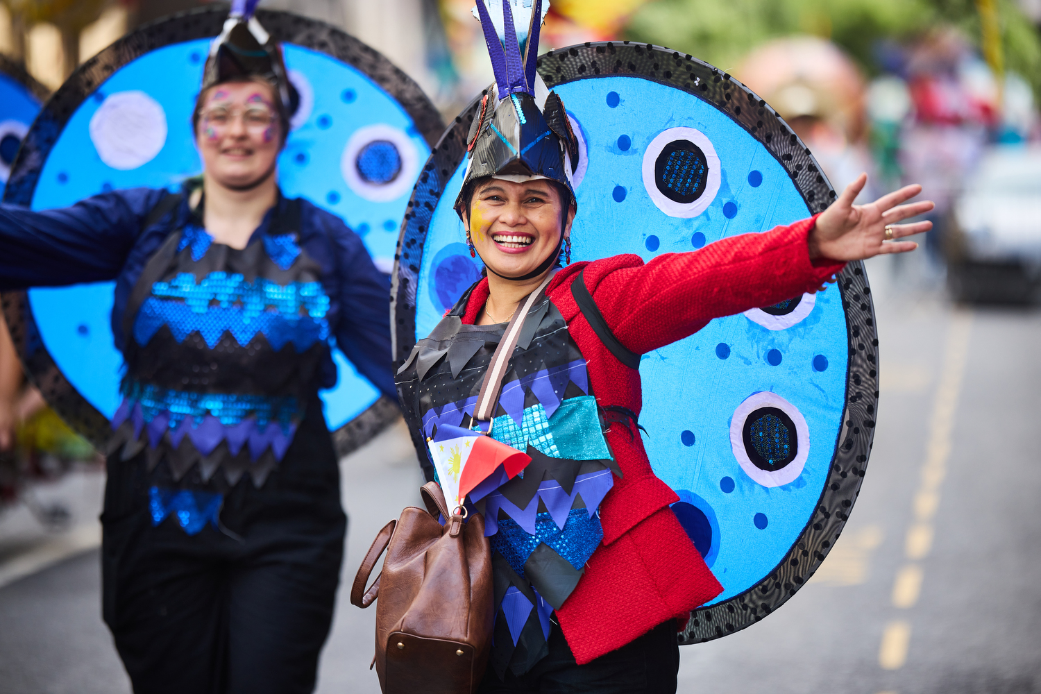 Two people dressed in blue, black and red costumes smiling in a parade