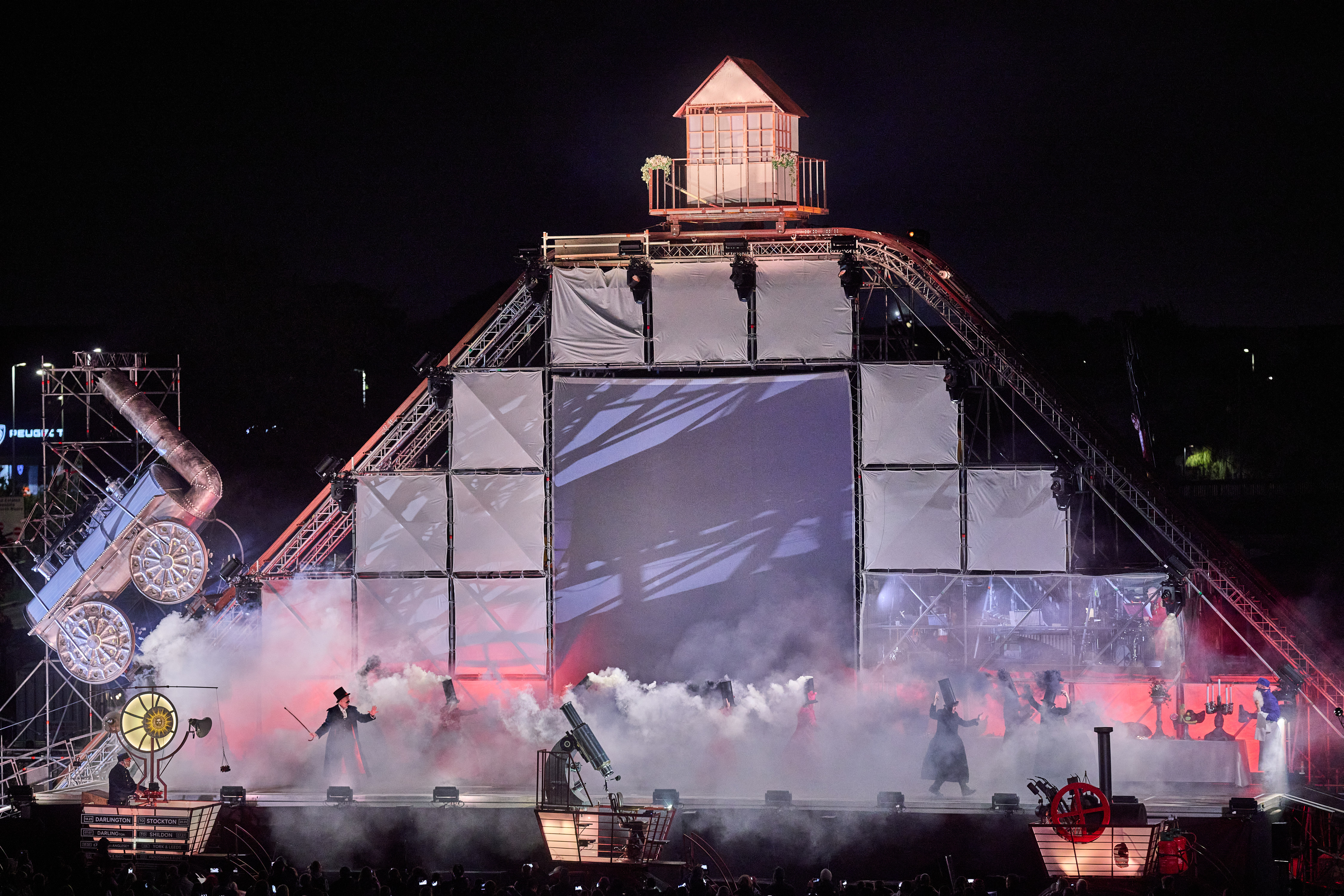 A huge triangle stage with a replica of a steam train in metal attached to tracks going along the sides. The stage filled with smoke. 