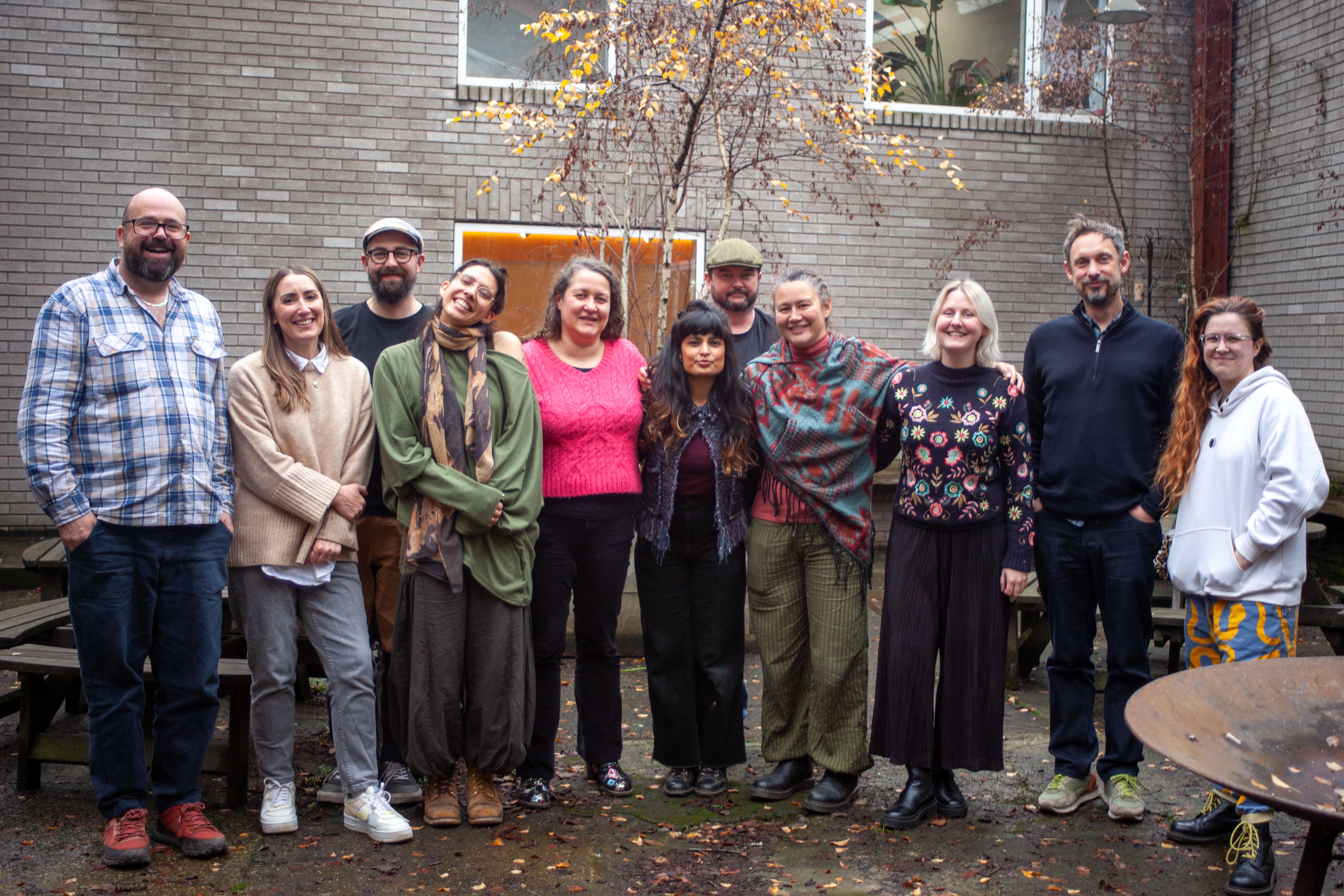 A group of 11 people standing out in a courtyard in autumn smiling at the camera. 