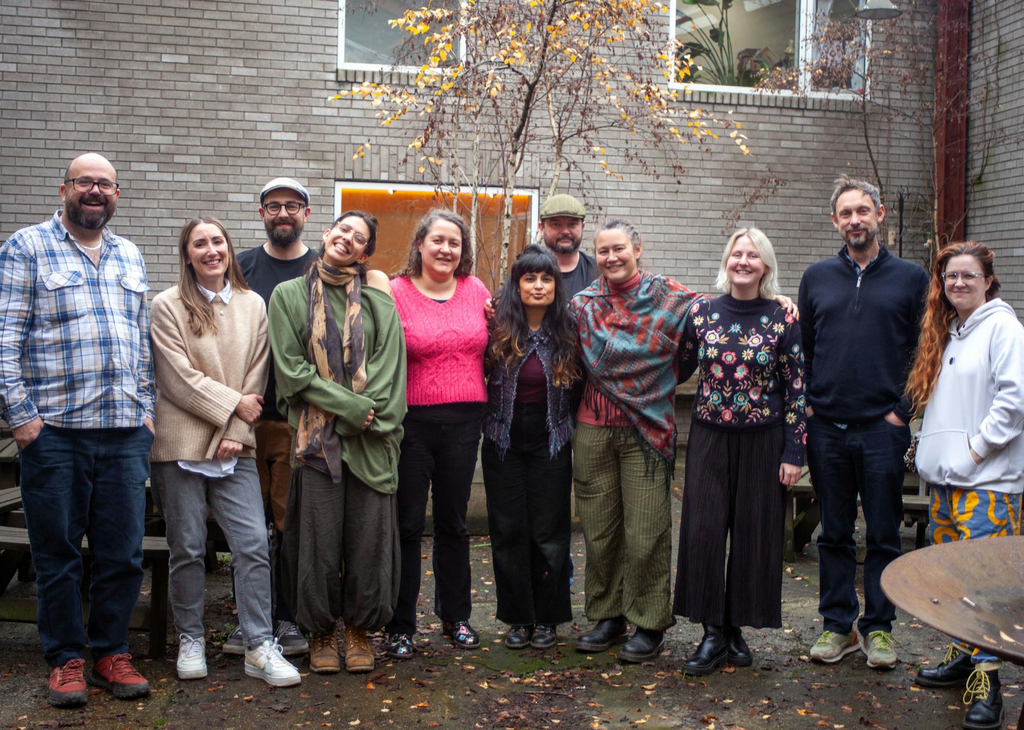 A group of 11 people standing out in a courtyard in autumn smiling at the camera.