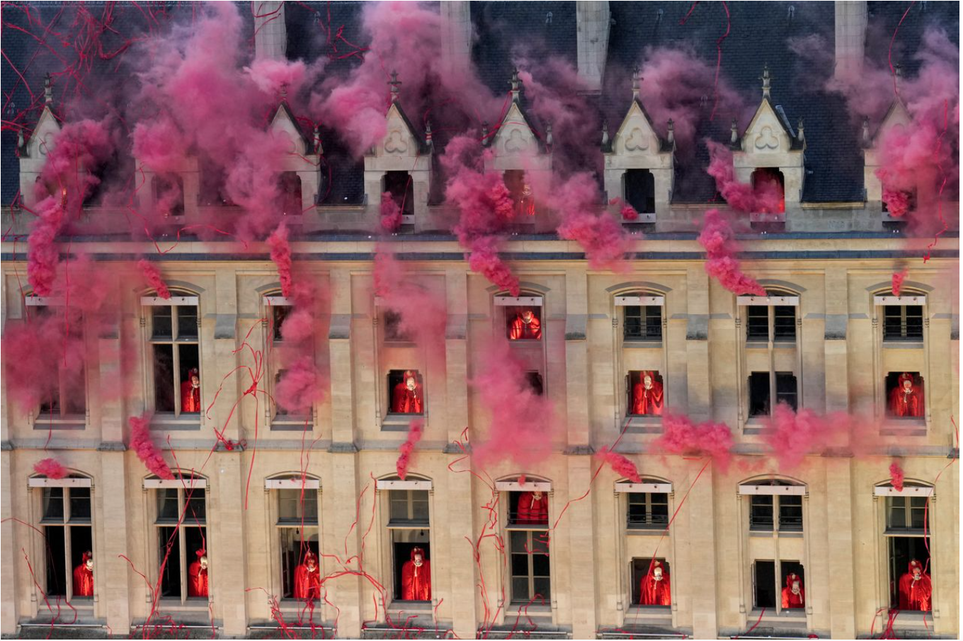 Actors in large bustling red gowns perform from 8 windows in the Gothic revival style. The actors are headless. Red streamers fill the foreground.
