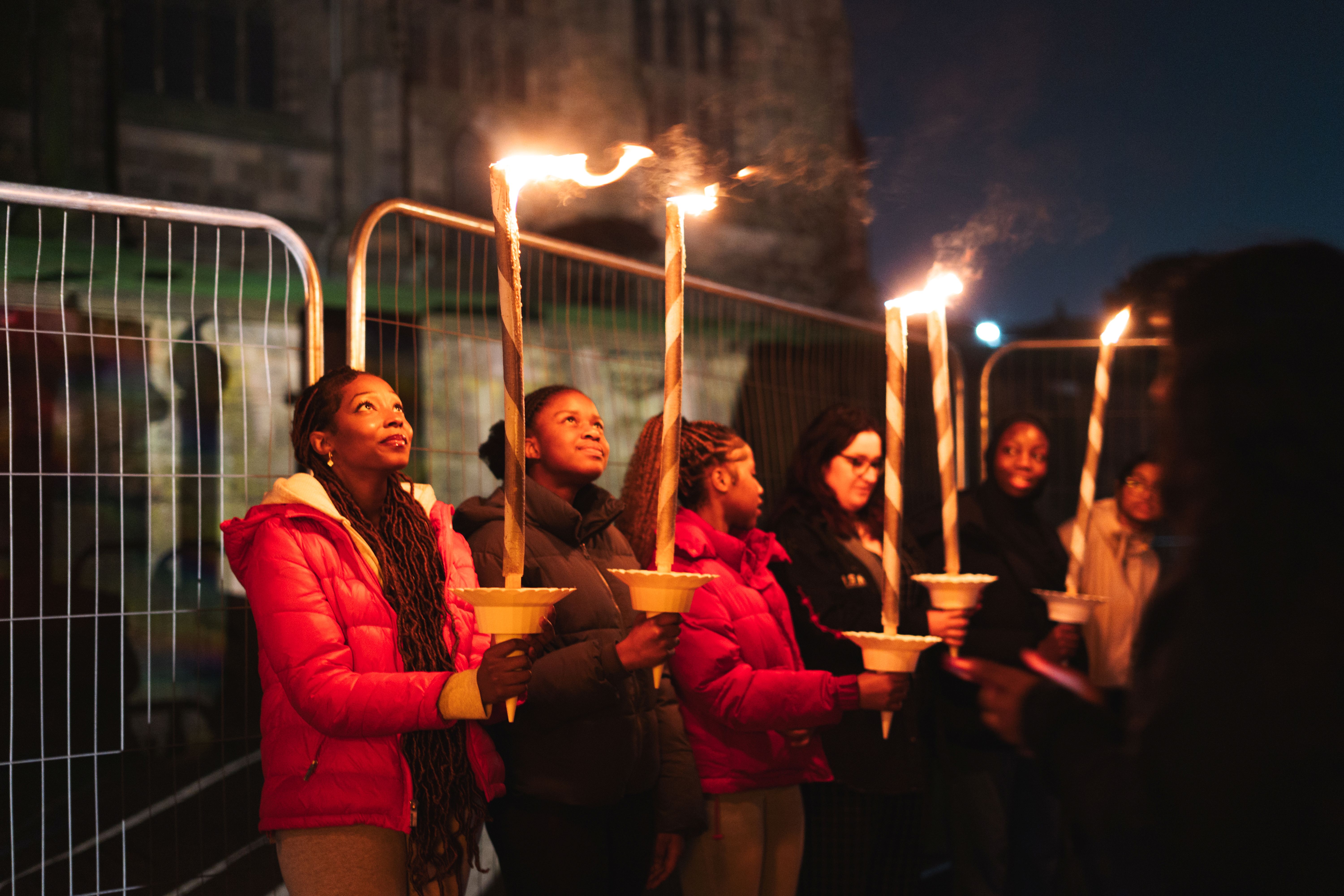 Group of people holding lit torches during a nighttime vigil or ceremony outdoors.