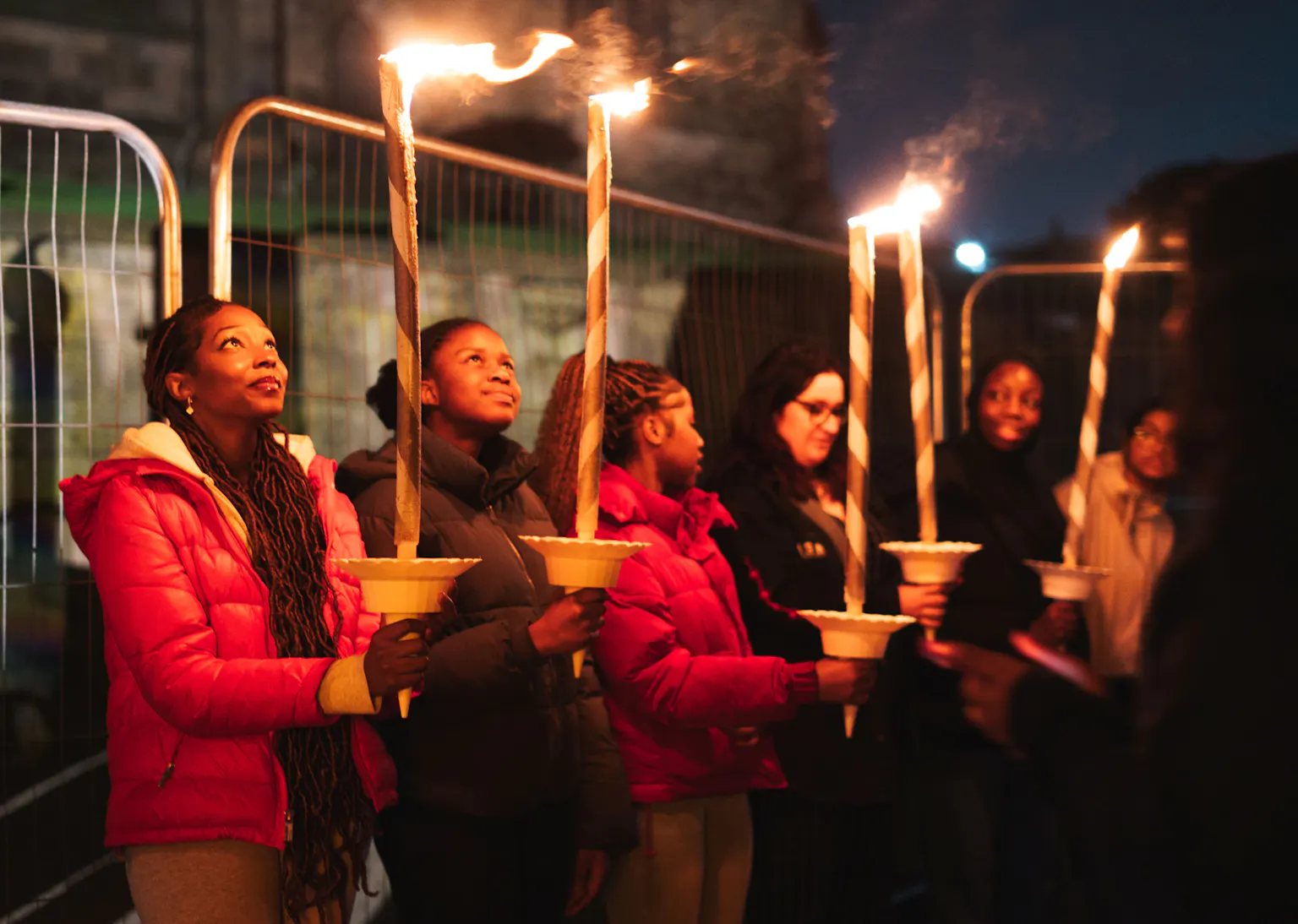 Group of people holding lit torches during a nighttime vigil or ceremony outdoors.