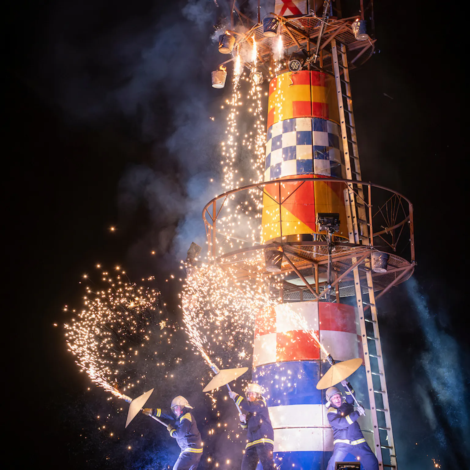 A large lighthouse structure with three lighthouse keeper performers on the structure with pyrotechnics