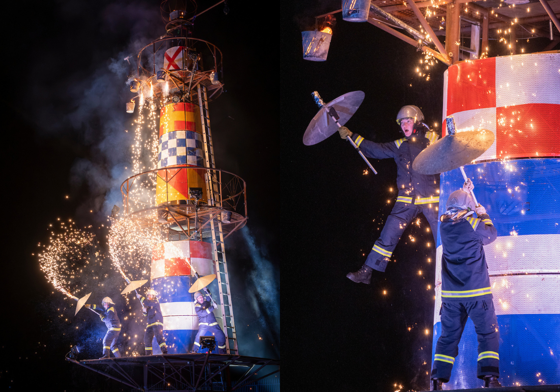 A large lighthouse structure with three lighthouse keeper performers on the structure with pyrotechnics