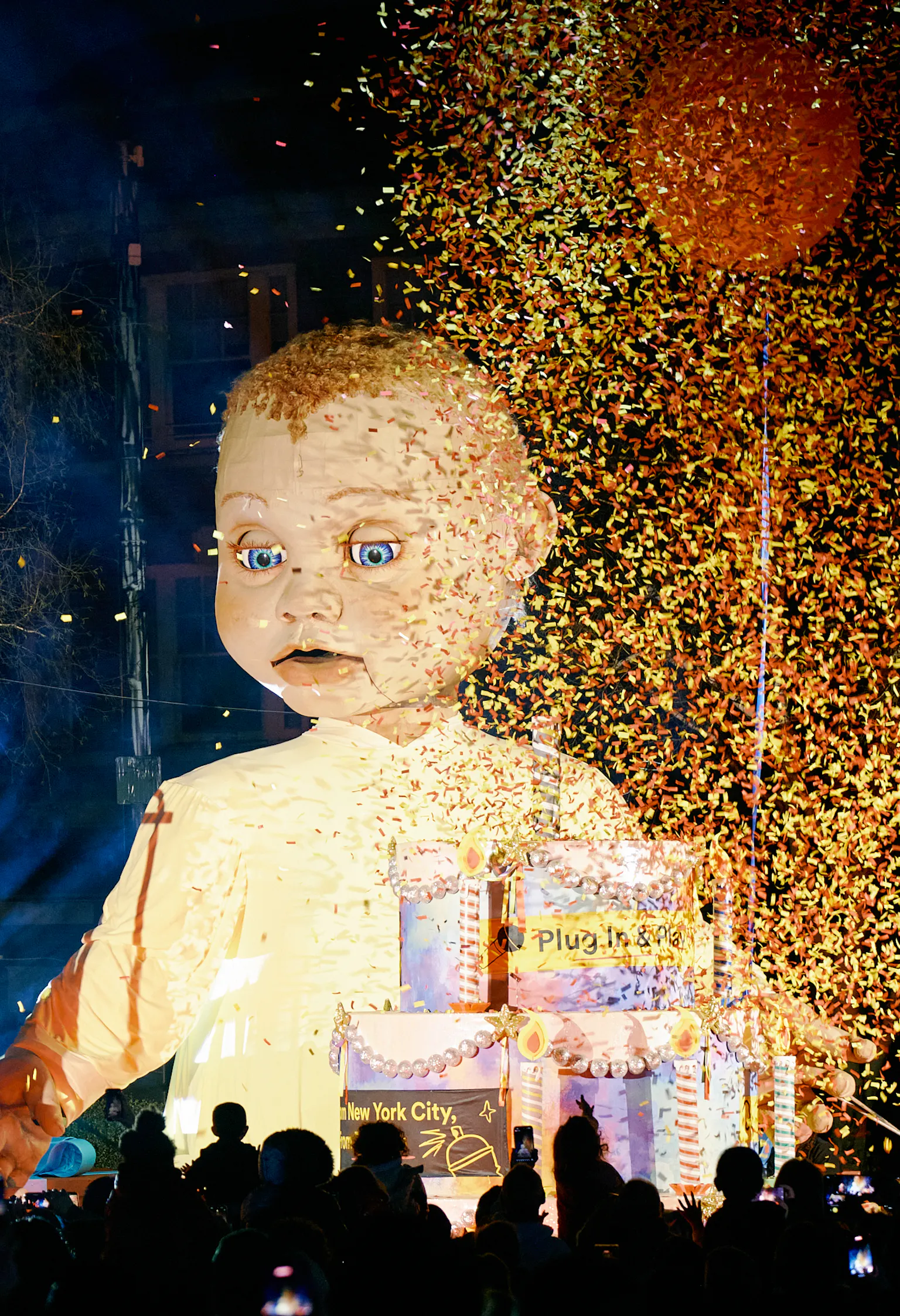 A large baby puppet is surronded by confetti and a singer.