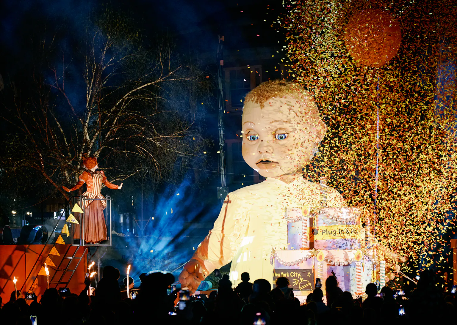 A large baby puppet is surronded by confetti and a singer.