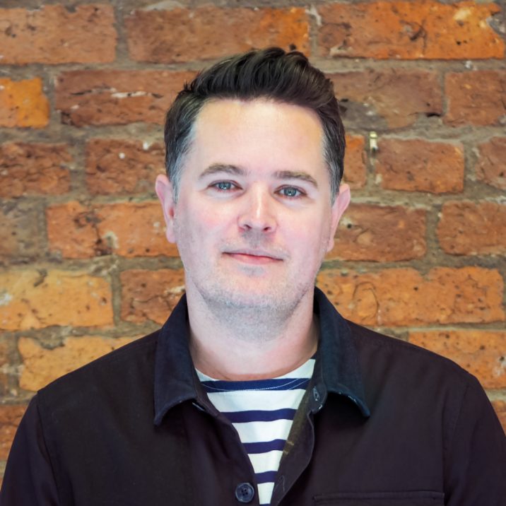 A white man with brown hair standing in front of a brick wall