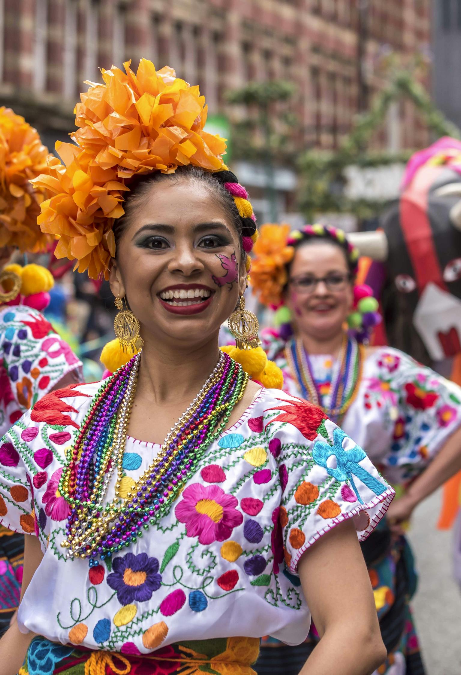 A group of Mexican dancers dressed up in colourful floral wear smiling. 